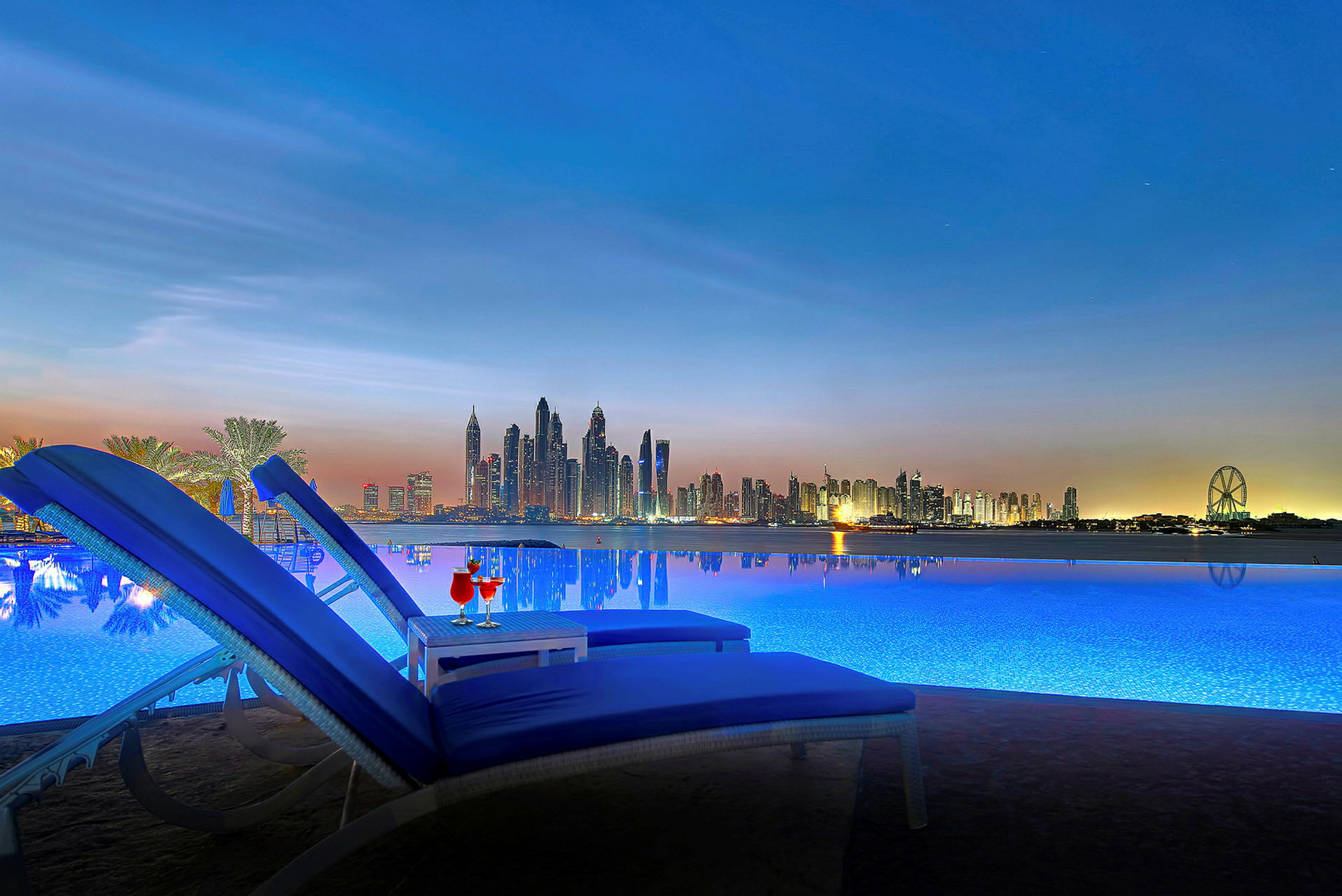 To solsenger ved et basseng med utsikt over en bysilhuett under skumringen. (AI-generert tekst)