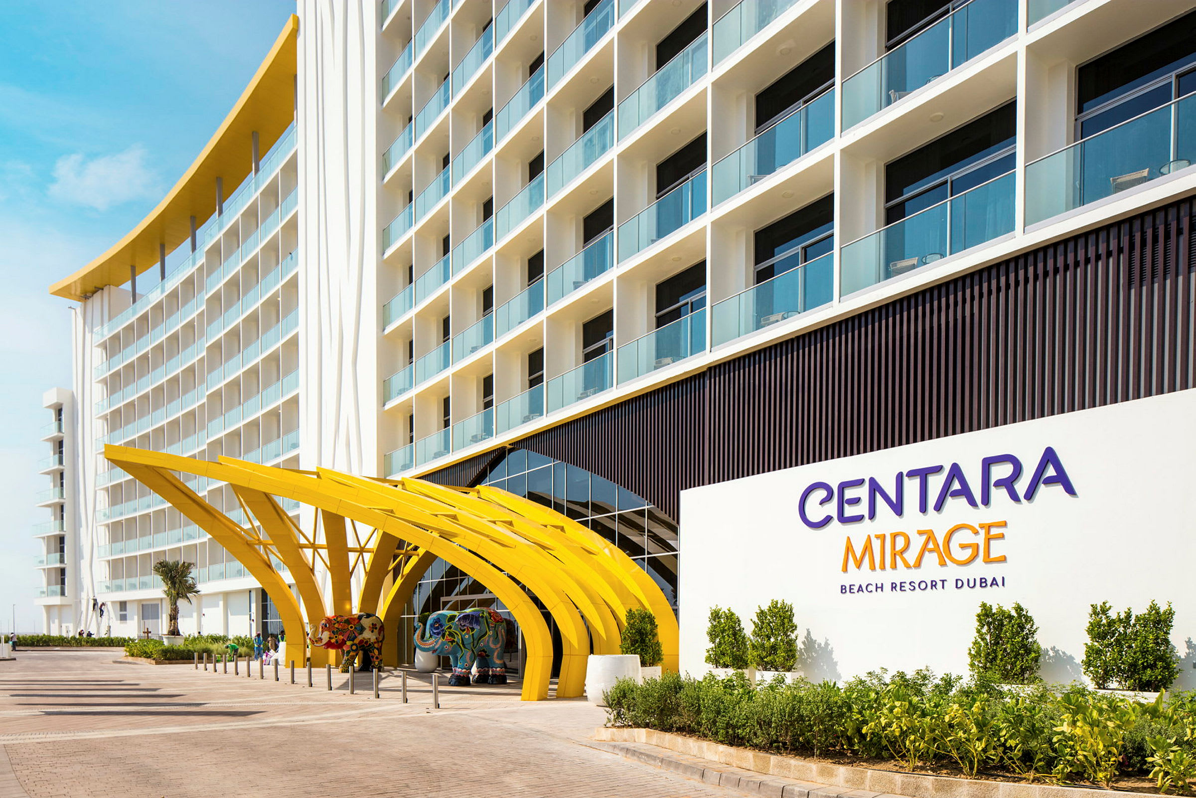 Inngangen til et hotell med buede gule strukturer og skilt som angir "Centara Mirage Beach Resort Dubai". (AI-generert tekst)