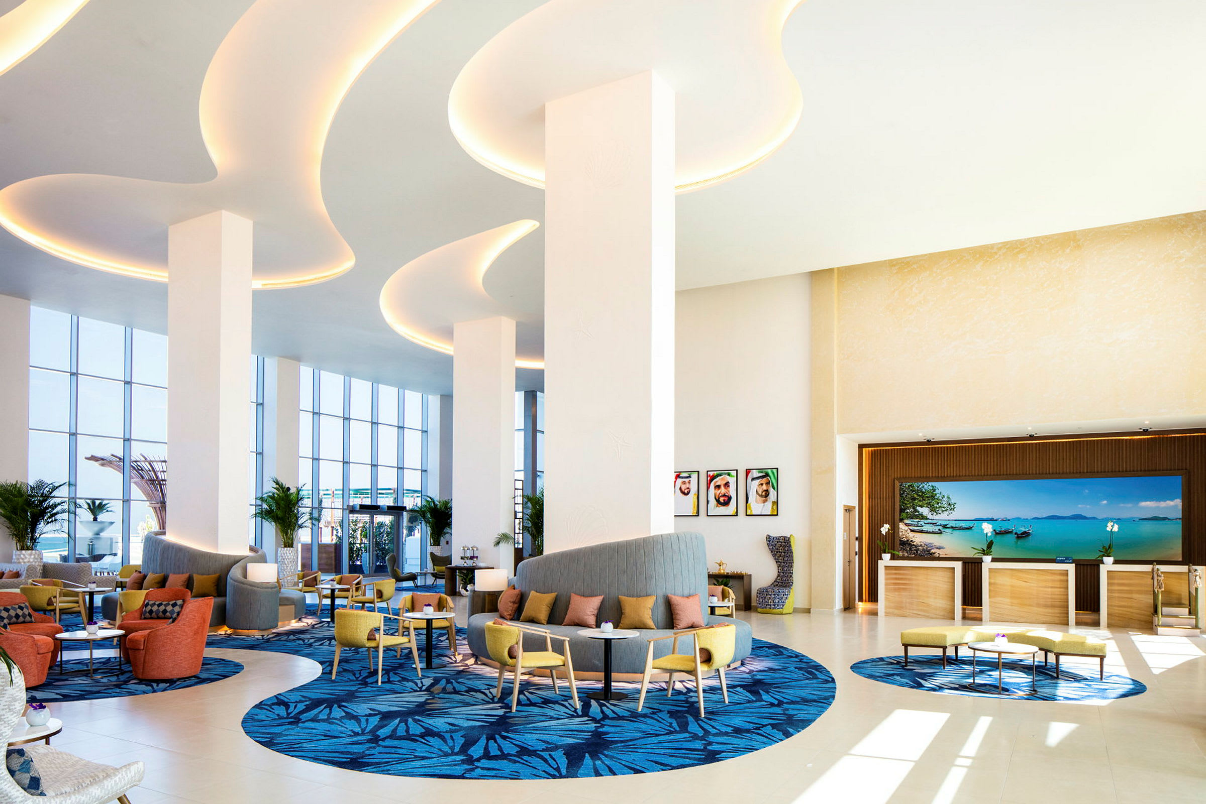 Lobbyen på et hotell med sitteplasser, dekorative tepper og store vinduer som slipper inn naturlig lys. (AI-generert tekst)