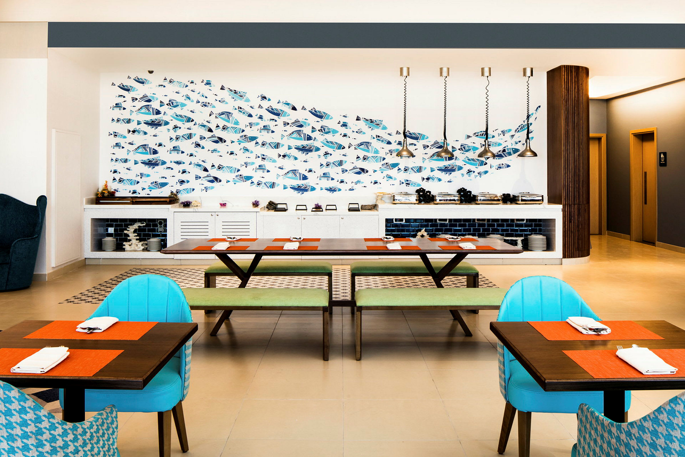En restaurant med et moderne innredet spiseområde som inkluderer bord med fargerike duker, stoler og en vegg med fiskemotiv. (AI-generert tekst)