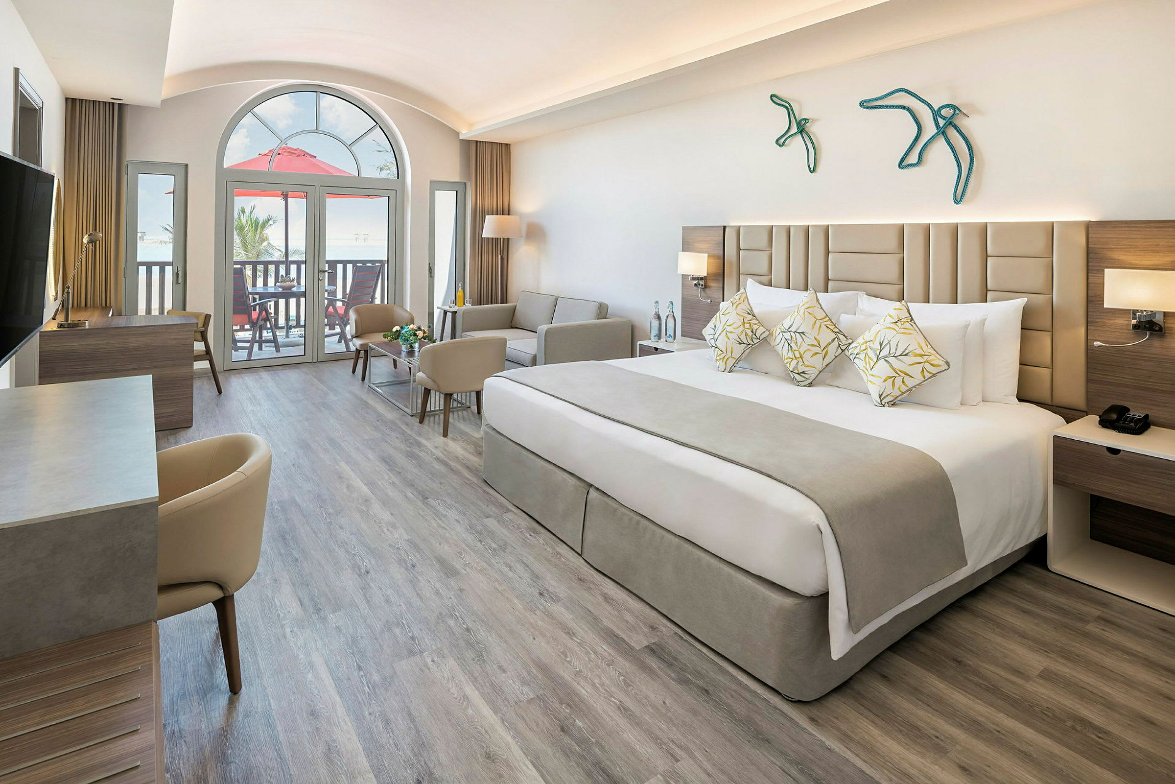Et moderne hotellrom med en bred seng, sofa og skrivebord. Stort vindu og balkong i bakgrunnen. (AI-generert tekst)