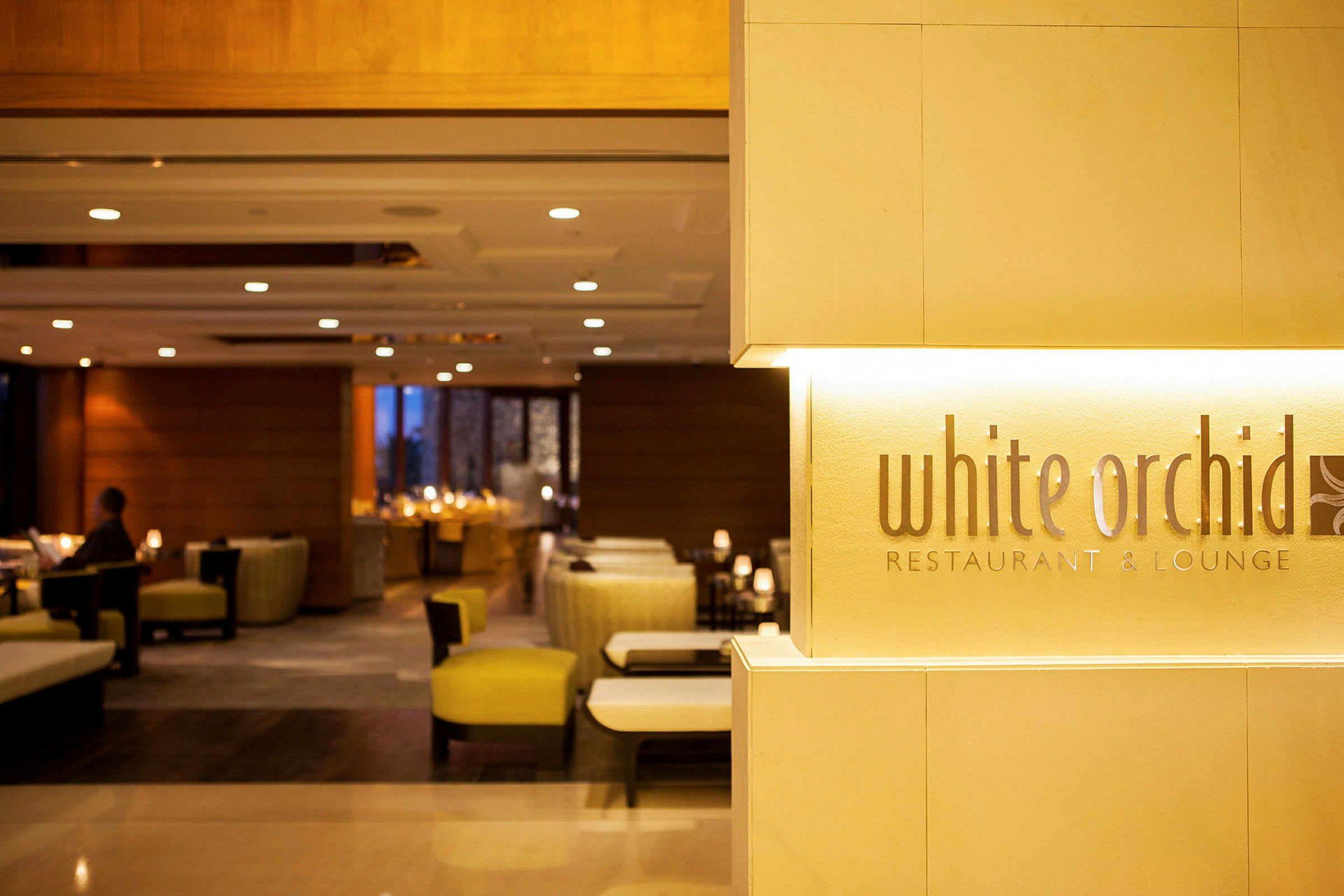 Skilt med teksten 'White Orchid Restaurant & Lounge' ved inngangen til en restaurant med moderne og elegant interiør. (AI-generert tekst)