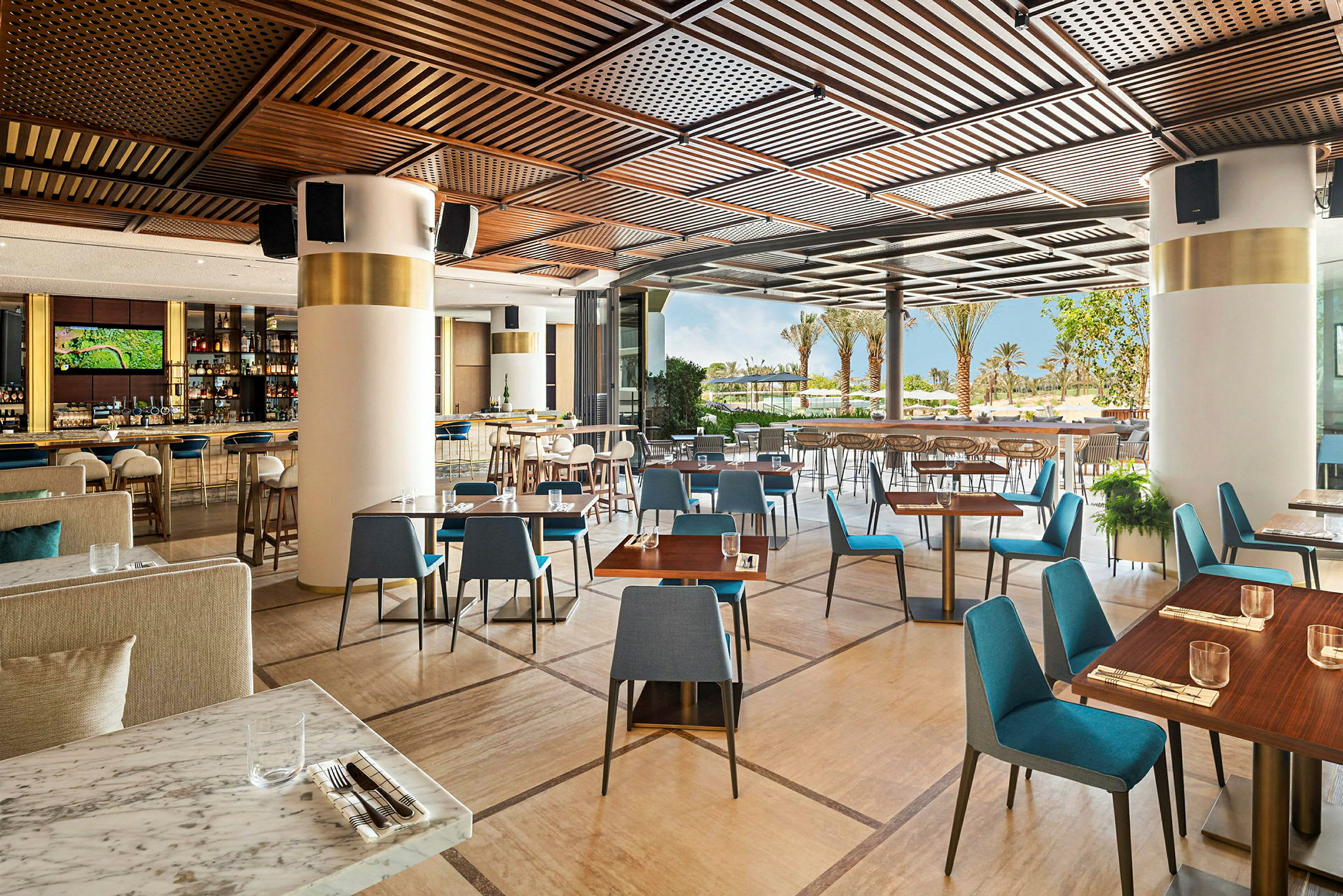 Restaurant med moderne bord og stoler samt åpning mot terrasse med utsikt over palmer og grøntområder. (AI-generert tekst)