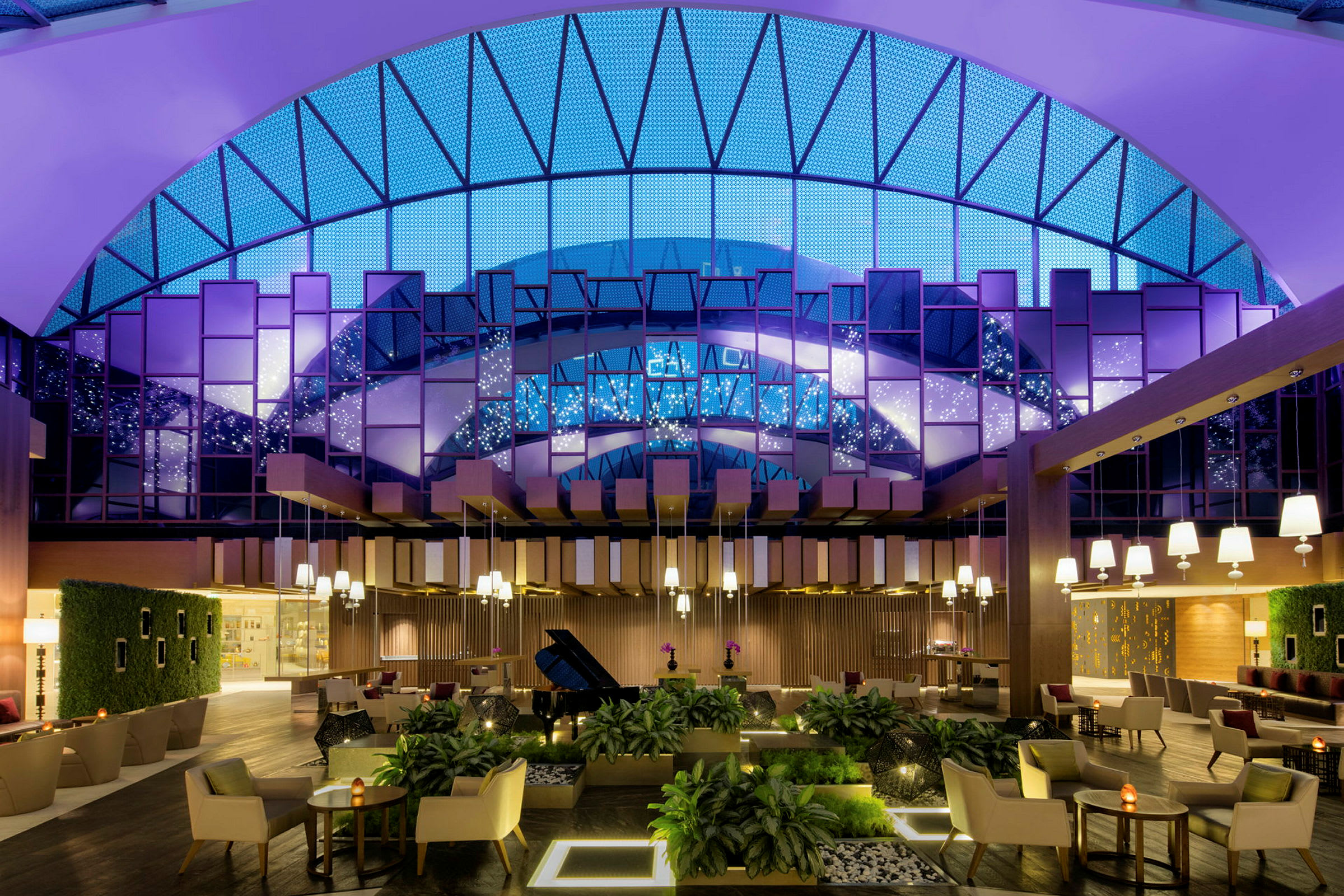 En elegant hotellobby med moderne møbler, planteinnredning og store vinduer med glødende belysning. (AI-generert tekst)