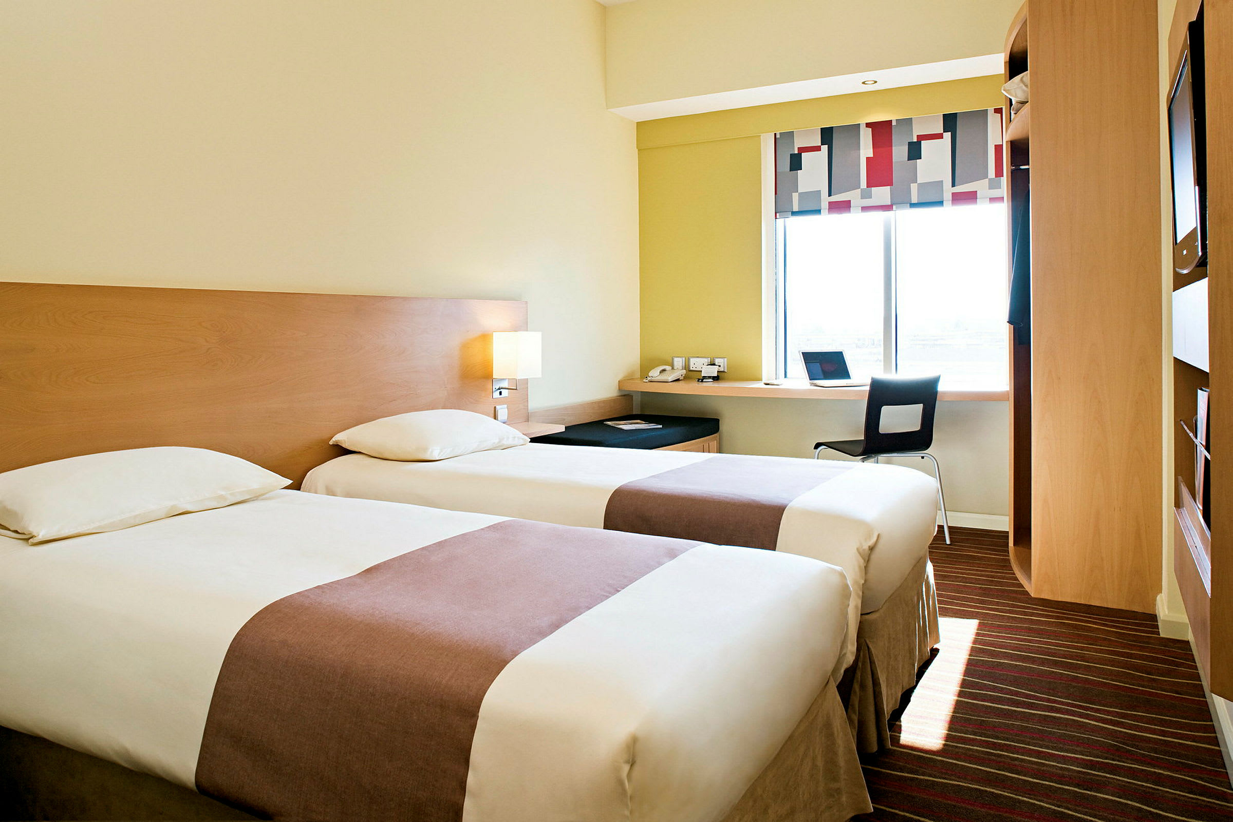 Et hotellrom med to enkeltsenger, en arbeidsstasjon ved et vindu og moderne møbler. (AI-generert tekst)