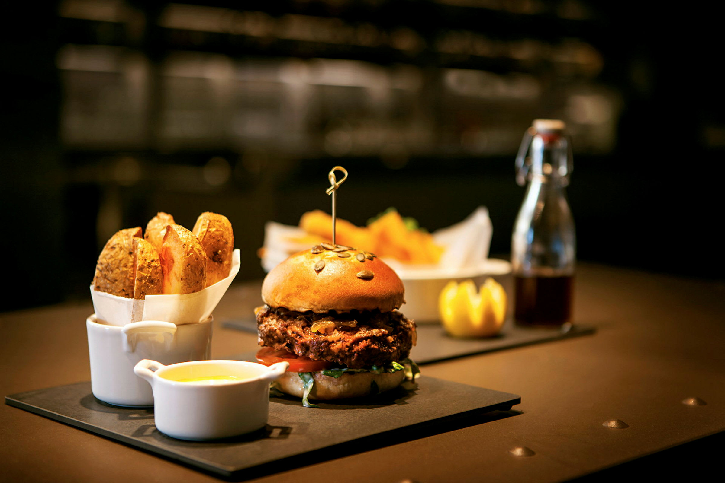 En hamburger med et brød med frø serveres på en tallerken med en skål med saus og pommes frites ved siden av. (AI-generert tekst)