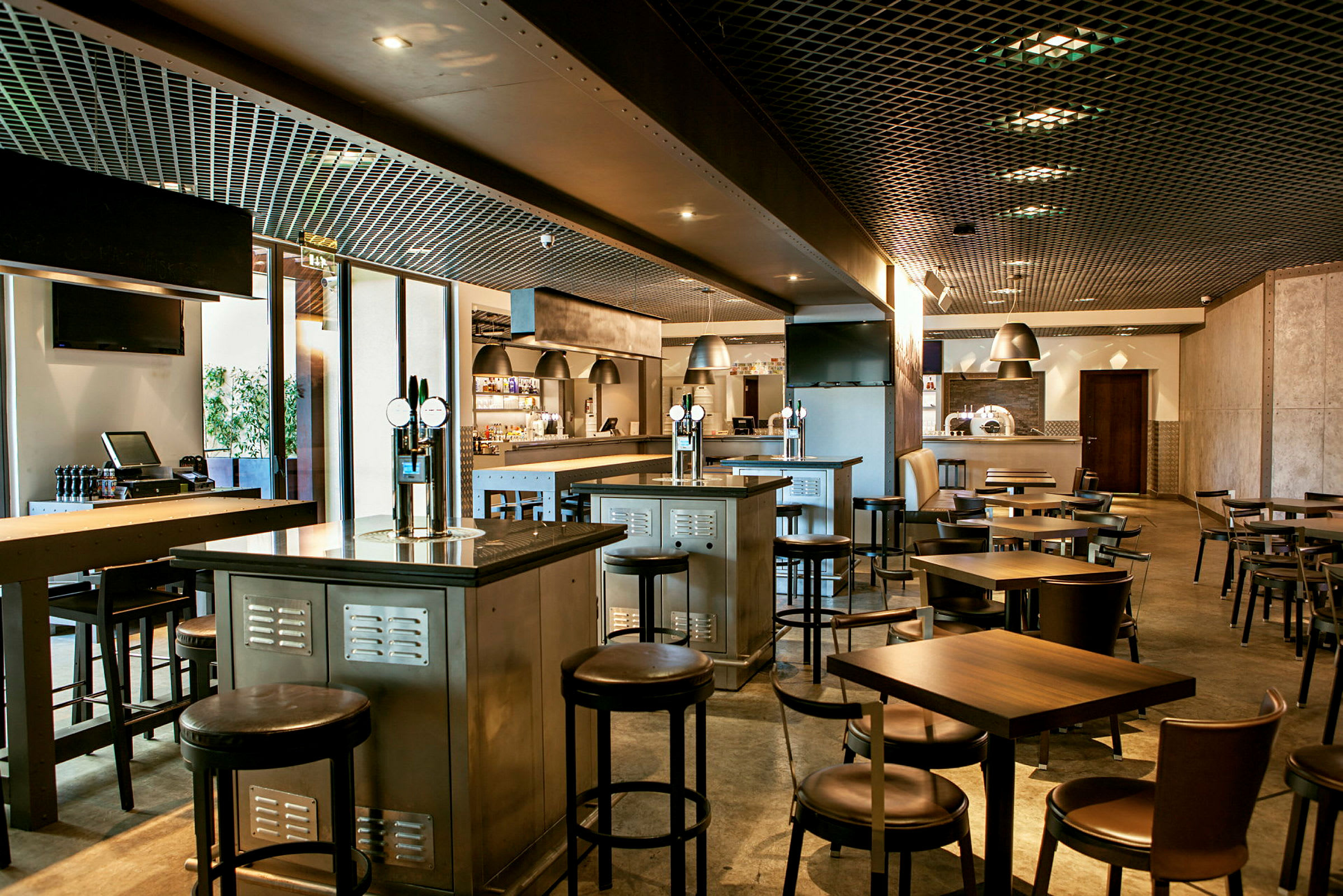 Et moderne restaurantinteriør med bord, stoler og bardisker. Belysningen er dempet, og interiøret har en industriell stil. (AI-generert tekst)