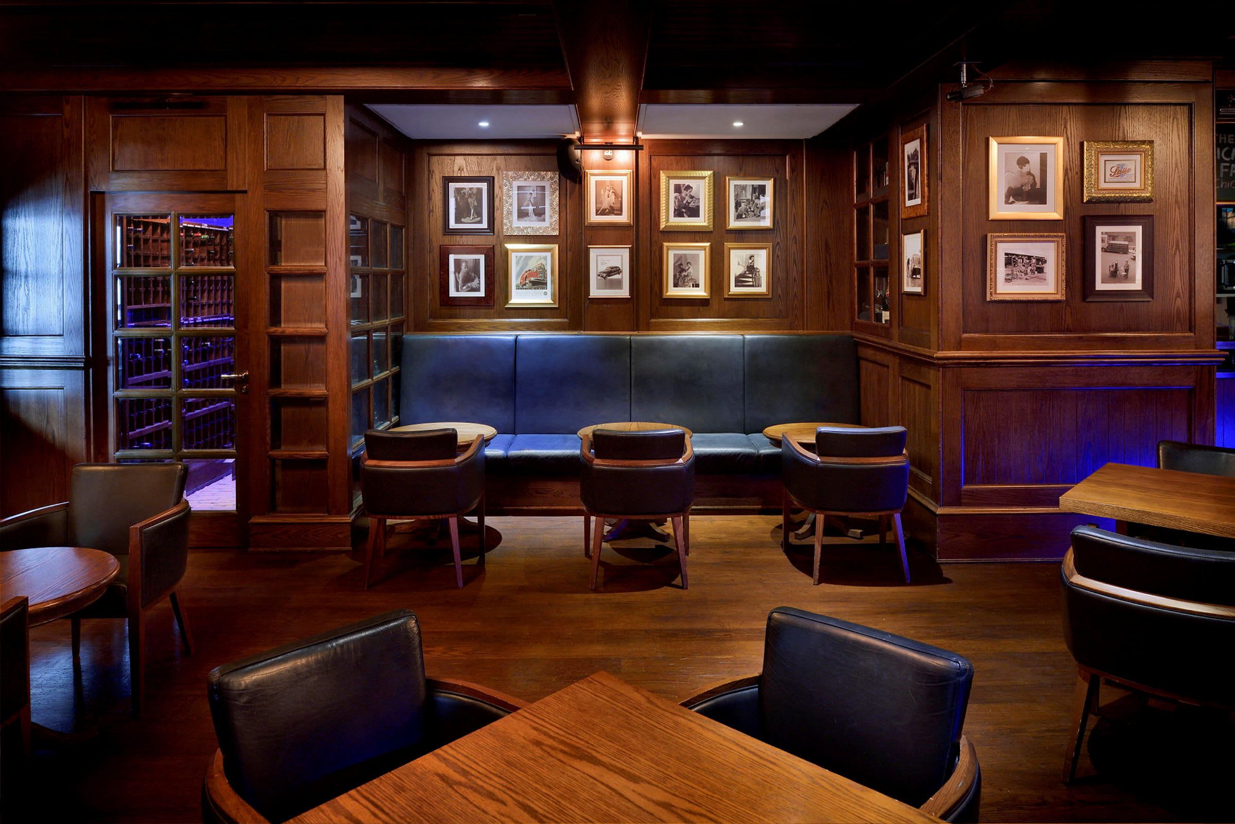Et rom innredet som en lounge eller bar med trepaneler, innrammede bilder på veggen, stoppede benker og stoler samt små bord. (AI-generert tekst)