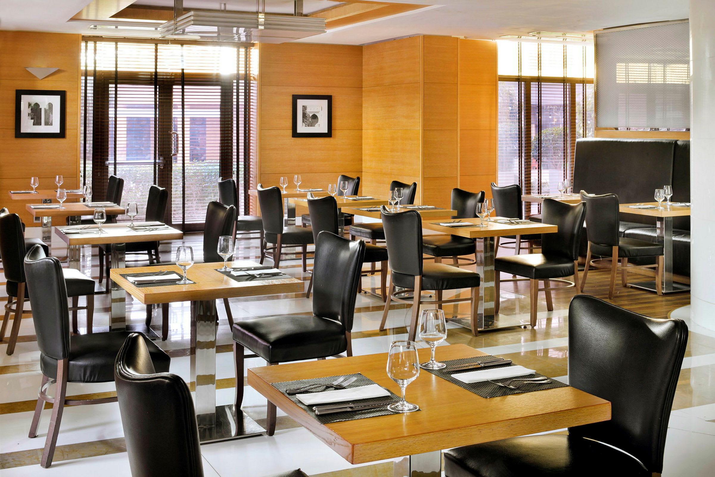 En restaurantlokale med bord og stoler i mørkt tre og lær, dekket med glass og servietter. (AI-generert tekst)