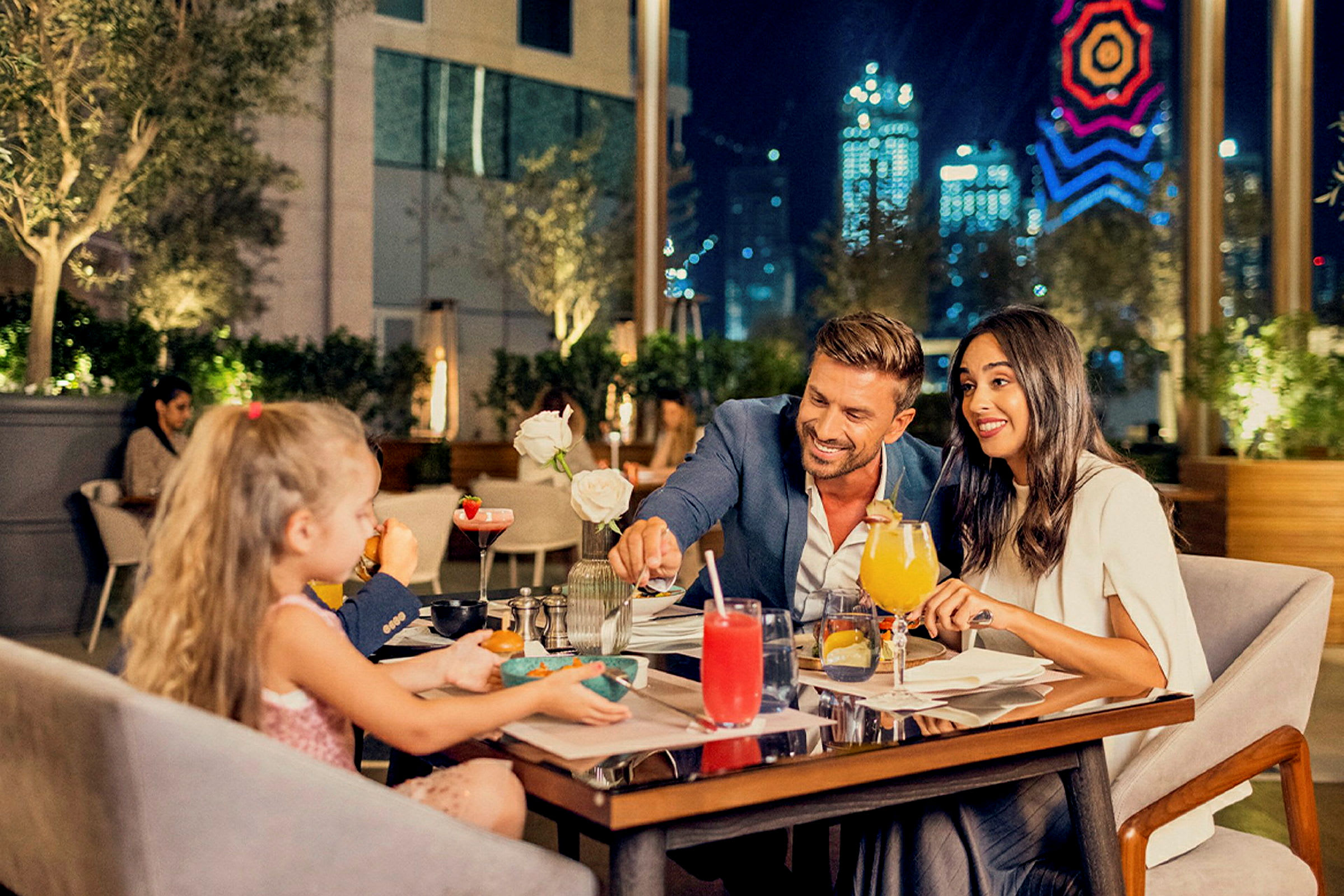 En middagscene på en restaurant med uteservering. Bakgrunnen viser moderne arkitektur og skinnende bylys. (AI-generert tekst)