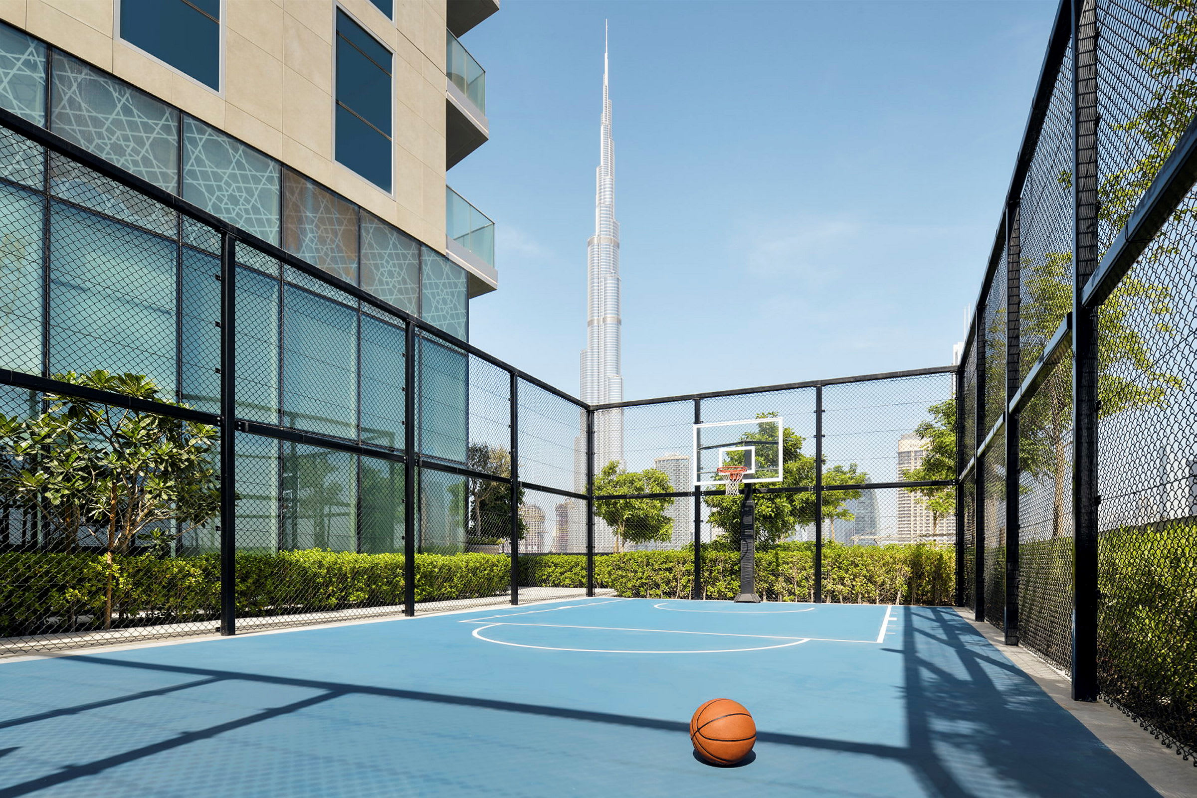 En basketballbane utendørs med en ball i forgrunnen og en moderne, høy bygning i bakgrunnen. (AI-generert tekst)
