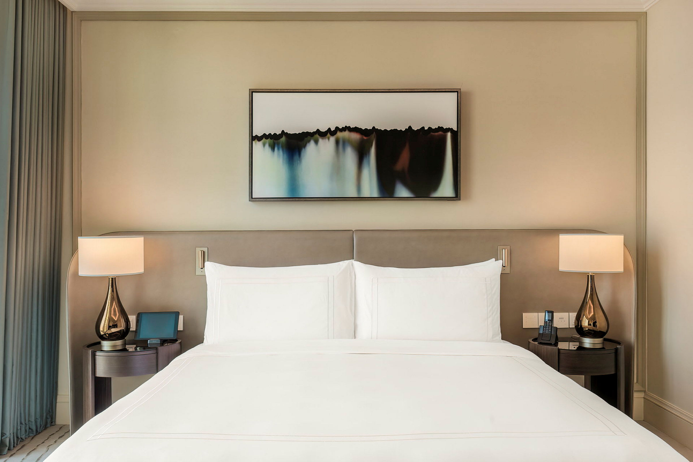 En velredt hotellseng med to nattbord og lamper på hver side, samt et bilde over sengens hodegavl. (AI-generert tekst)