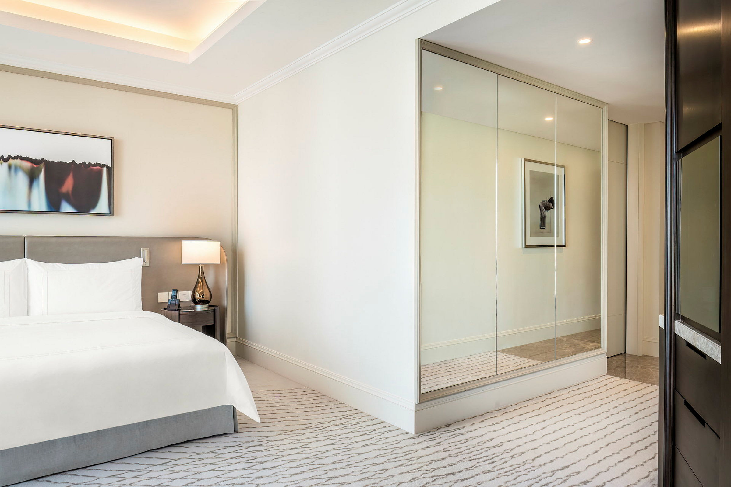 Et moderne og lyst hotellrom med en dobbeltseng, en lampe på et nattbord og en speilvegg. (AI-generert tekst)