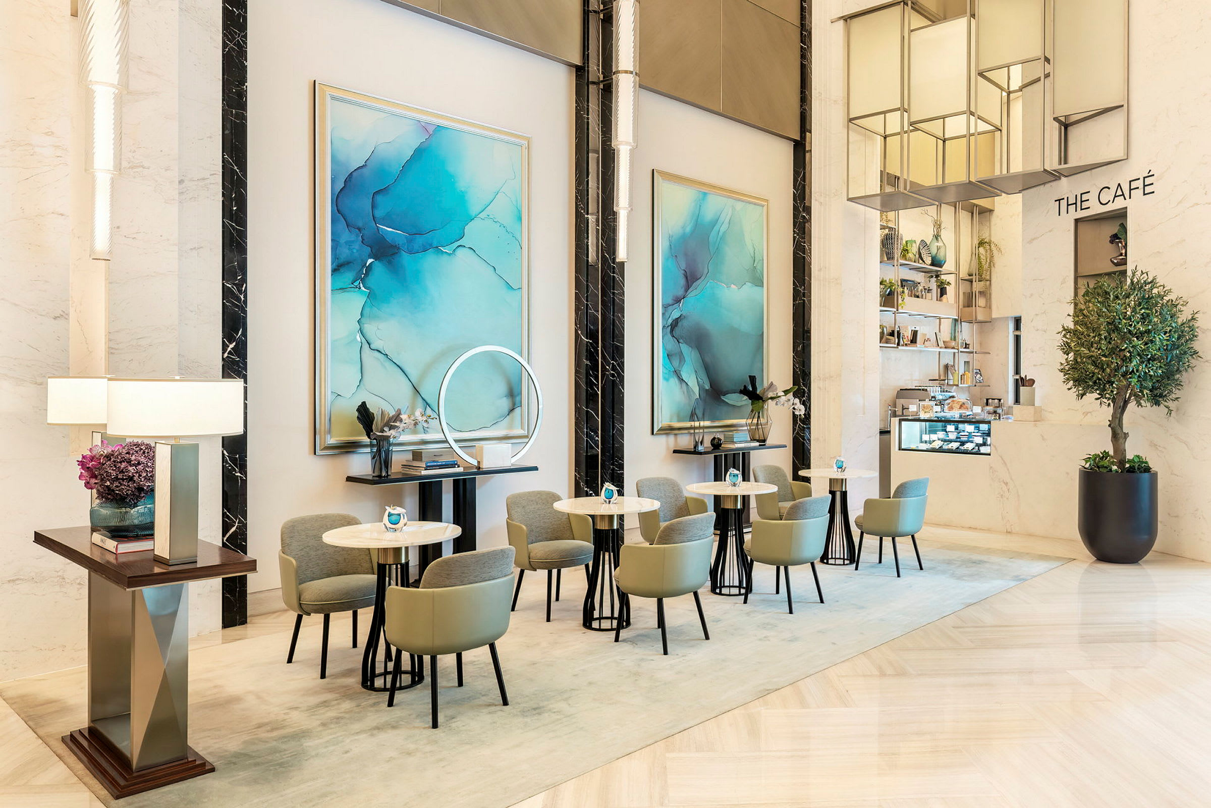 Et moderne elegant kafé med små bord og stoler i et lyst interiør, dekorert med blå abstrakt kunst på veggene. (AI-generert tekst)