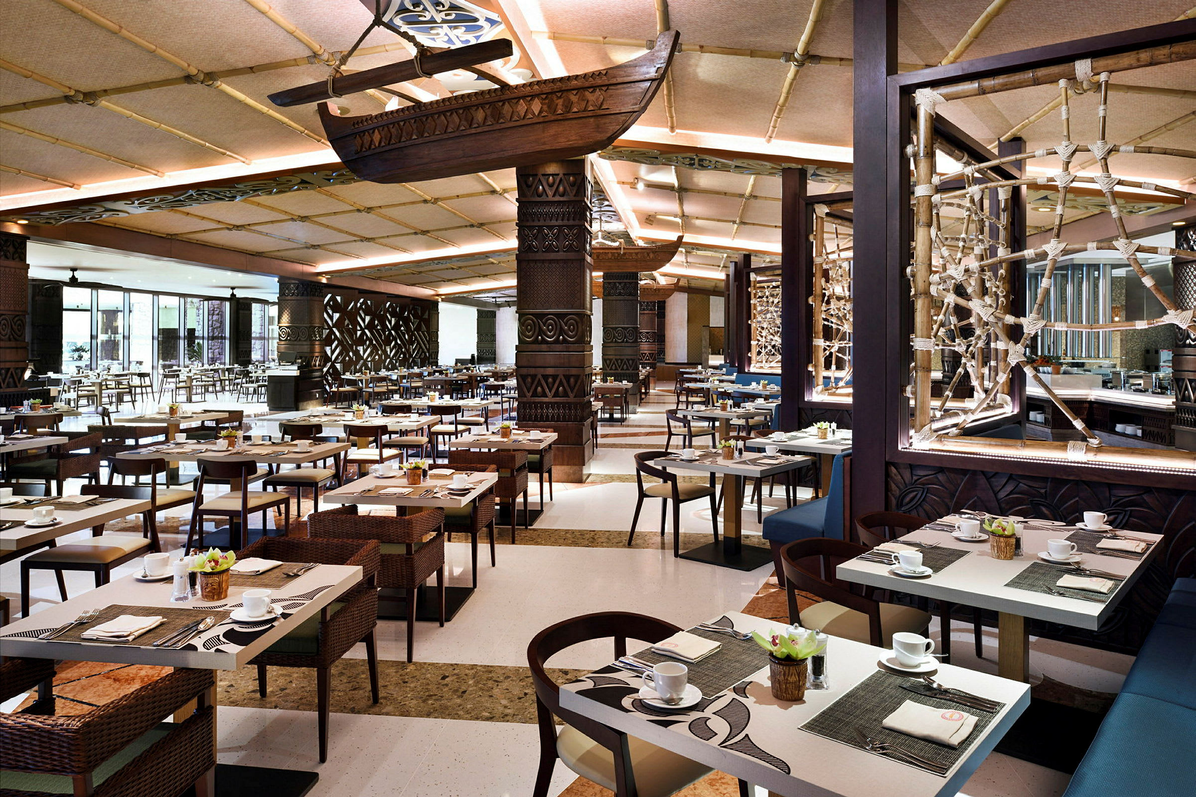 Innredning i en romslig restaurant med bord dekket for måltider, dekorative tak og vegger. Et skip henger fra taket som en del av dekoren. (AI-generert tekst)