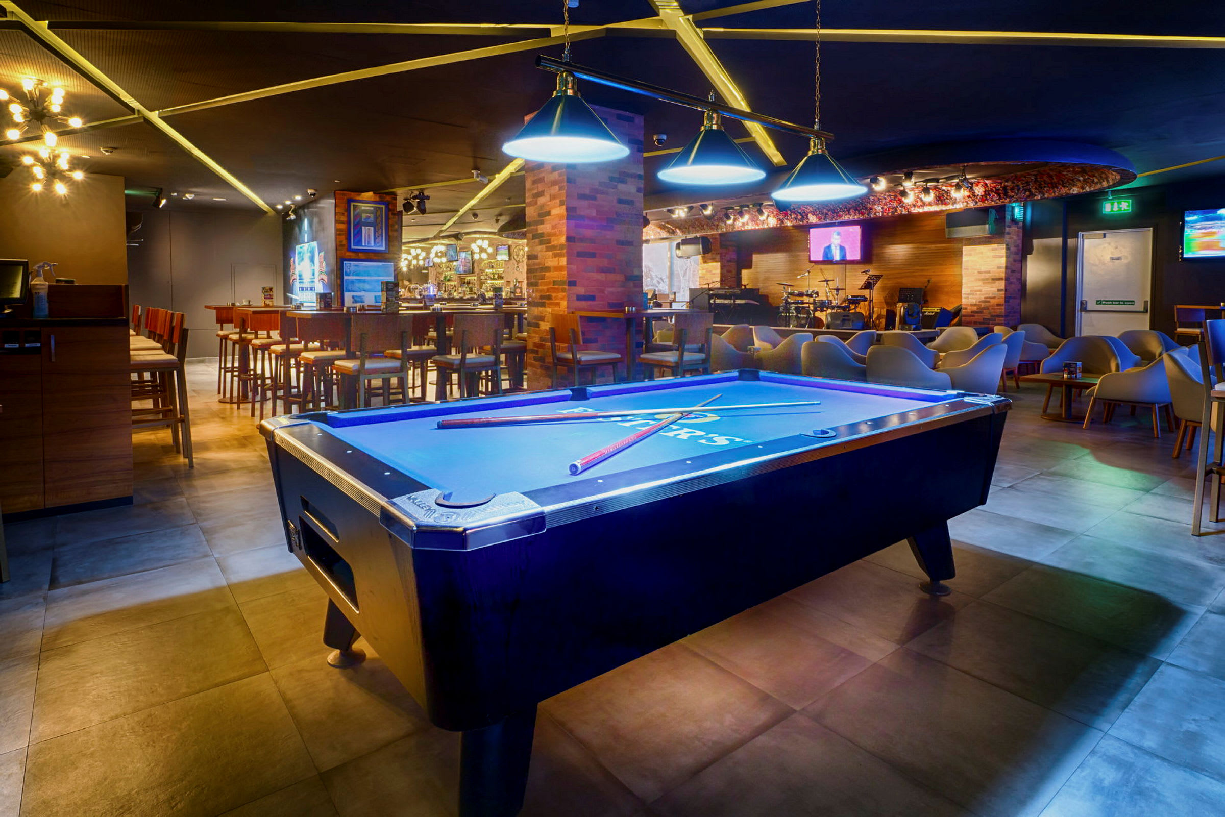 Biljardbord i en fargerikt opplyst lounge med bar og sitteplasser. (AI-generert tekst)