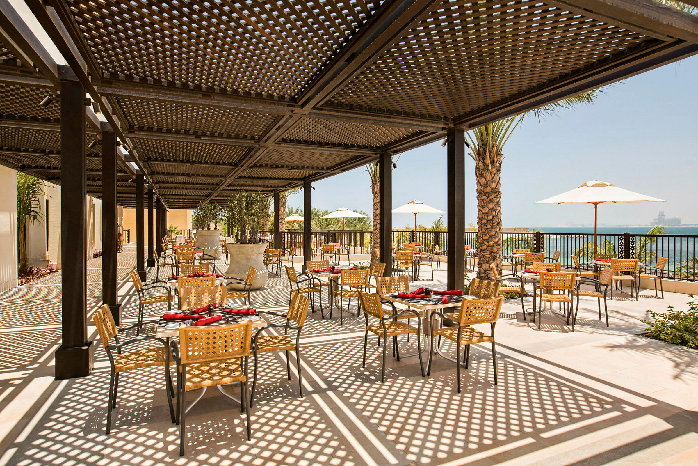 Utendørsrestaurant med bord og stoler under skyggefull pergola. (AI-generert tekst)
