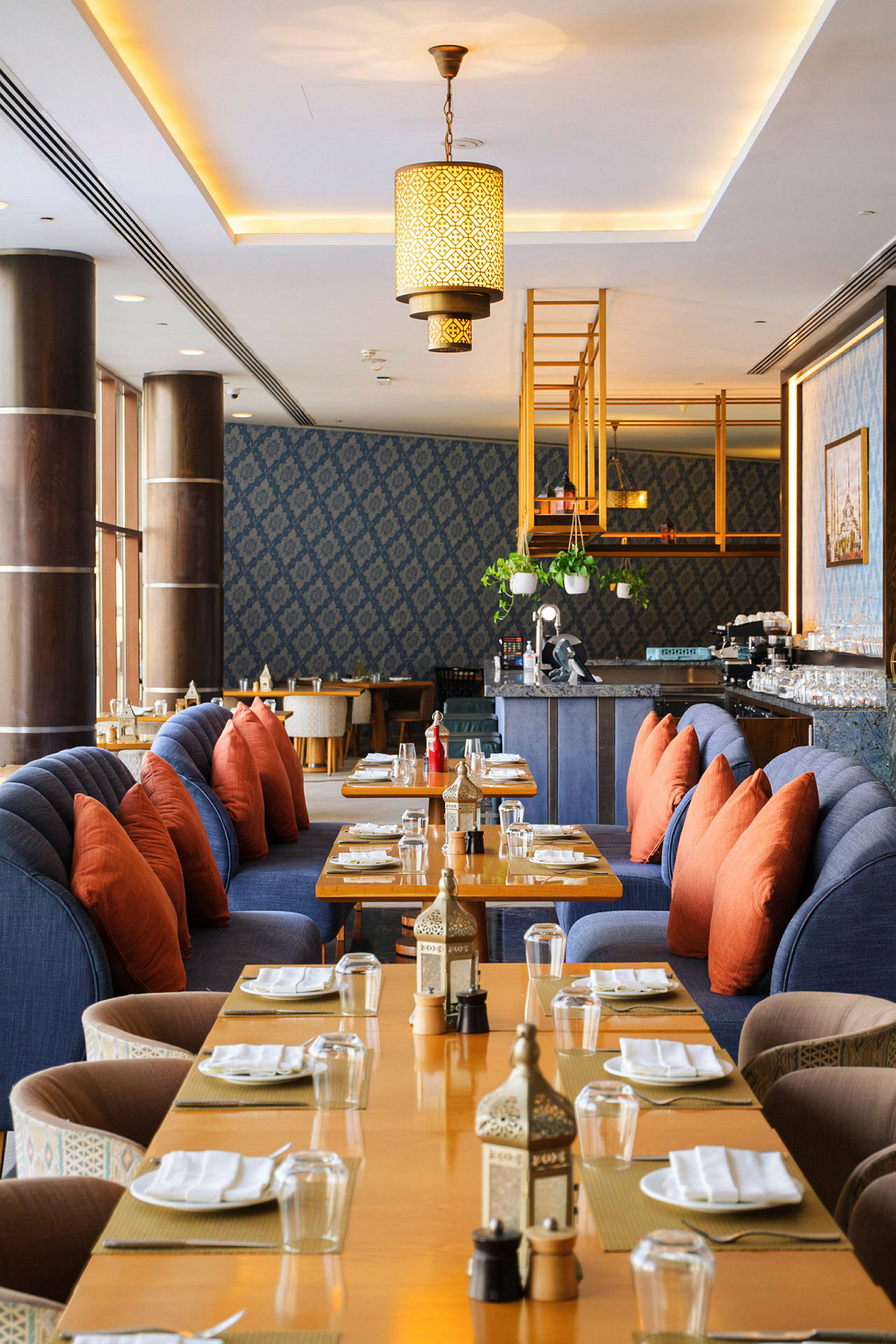 En restaurant med dekkede bord, blå sofaer og oransje puter. (AI-generert tekst)