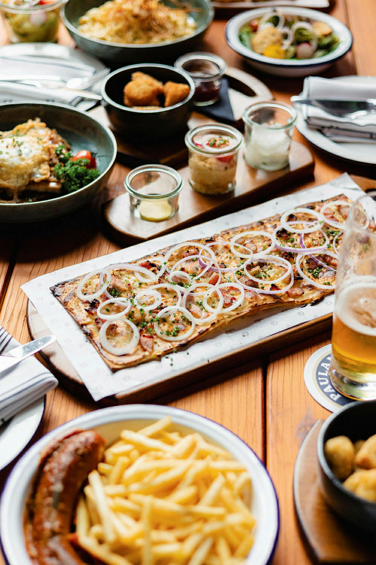 Et bord satt med forskjellige retter, inkludert en pizza med løk, pommes frites og en pølse. (AI-generert tekst)