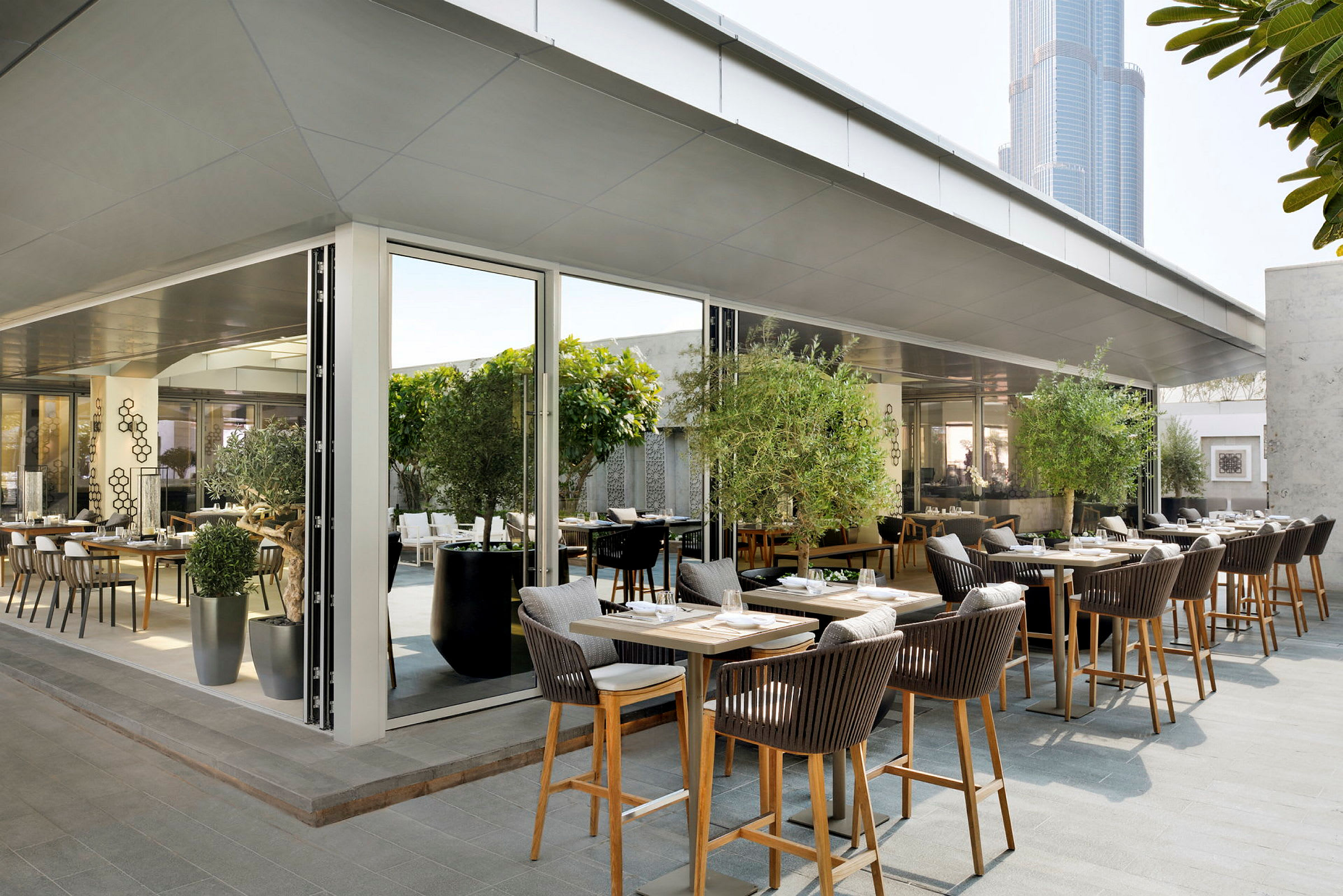 En moderne restaurant med sitteplasser utendørs dekorert med grønne planter og moderne møbler. (AI-generert tekst)