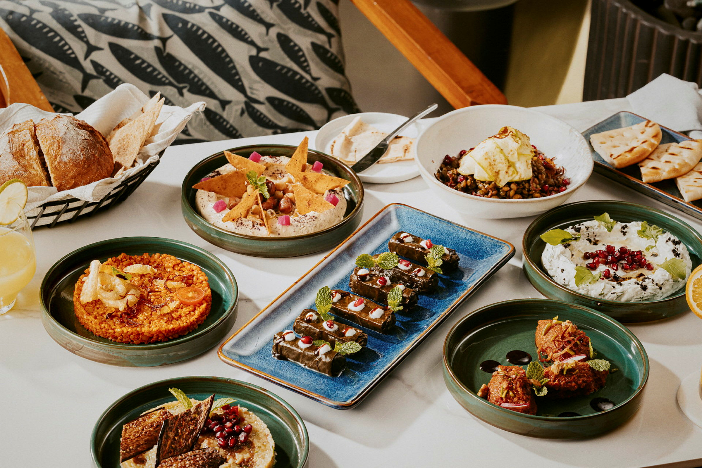 Et bord med forskjellige retter, inkludert brød, hummus, salat og dolma, servert på tallerkener. (AI-generert tekst)