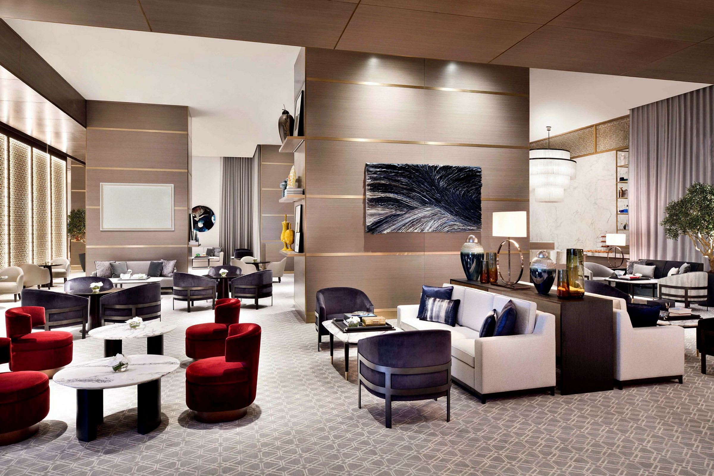 En elegant hotellobby med moderne møbler, inkludert sofaer, lenestoler og salongbord. Rommet har interiørdetaljer som kunstverk på veggen, belysning og dekorative gjenstander. (AI-generert tekst)