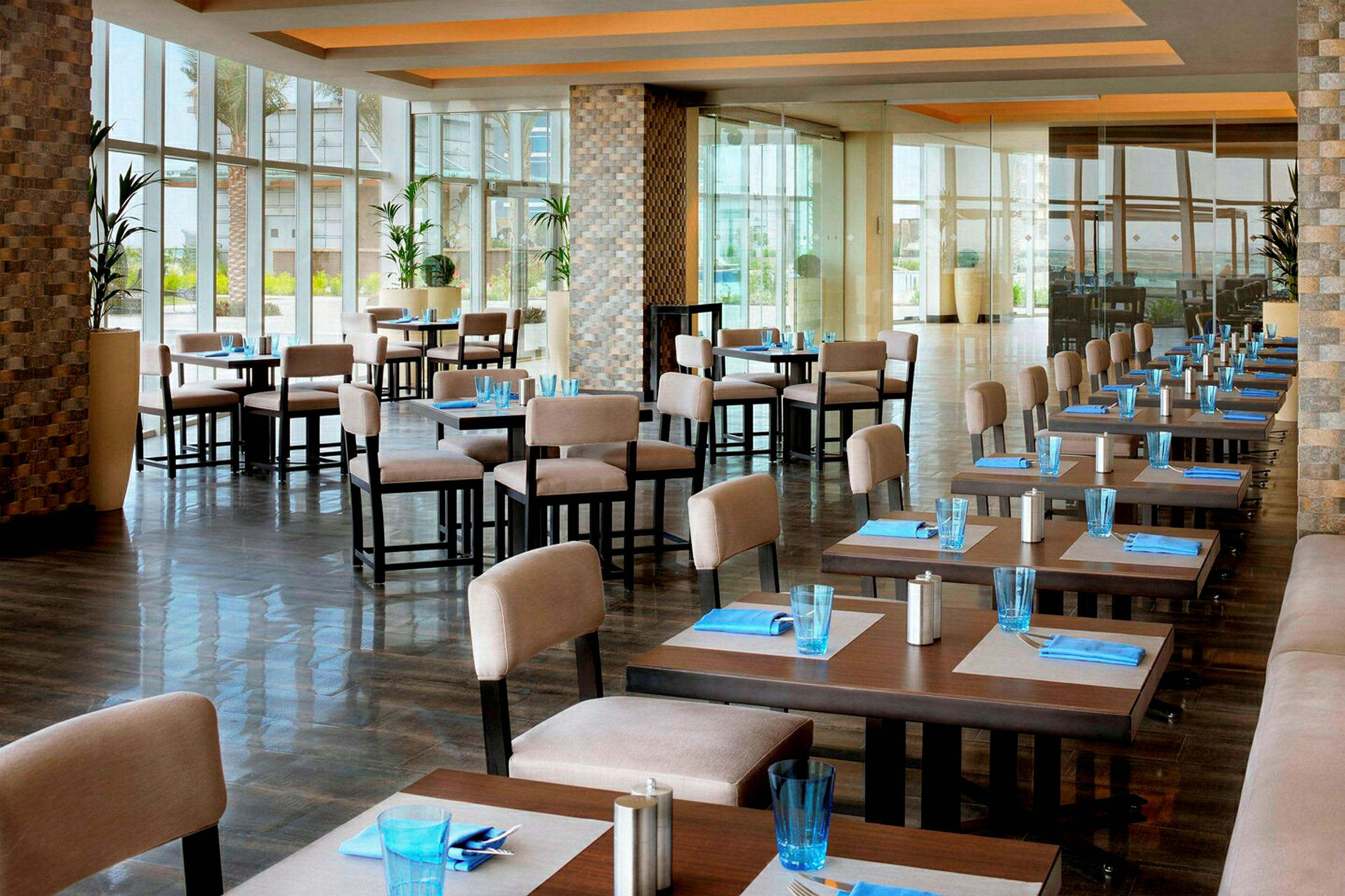 En åpen restaurant med dekkede bord, lyse stoler og store vinduer. (AI-generert tekst)