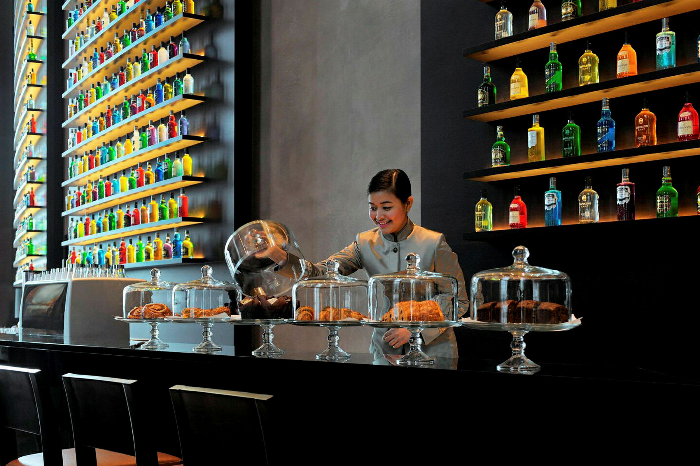 En moderne kafé med glassmontrer som viser bakverk og en vegg fylt med dekorative flasker. (AI-generert tekst)
