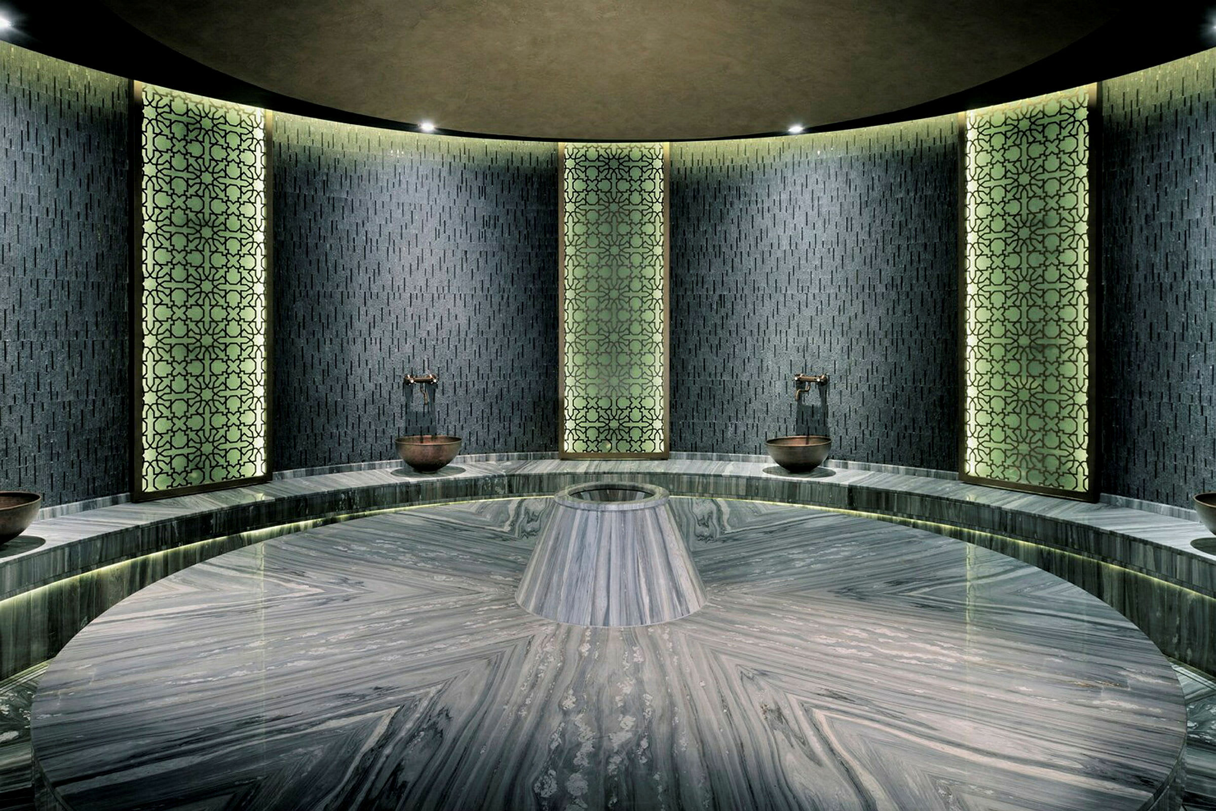 Et moderne utformet hamam med mønstrede veggpaneler og en rund marmorplattform i midten. (AI-generert tekst)