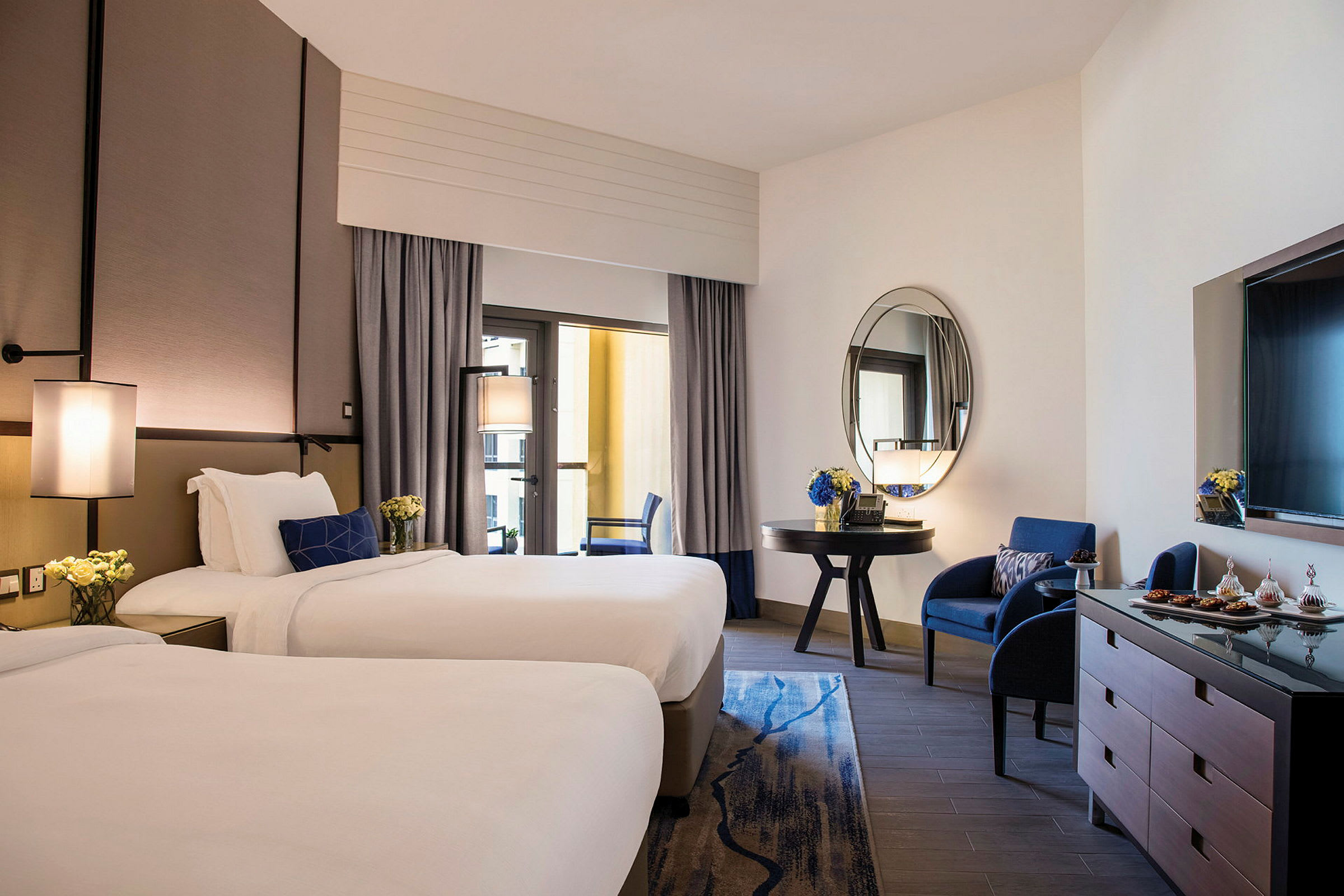 Hotellrom med to enkeltsenger, en sittegruppe og et speil. (AI-generert tekst)