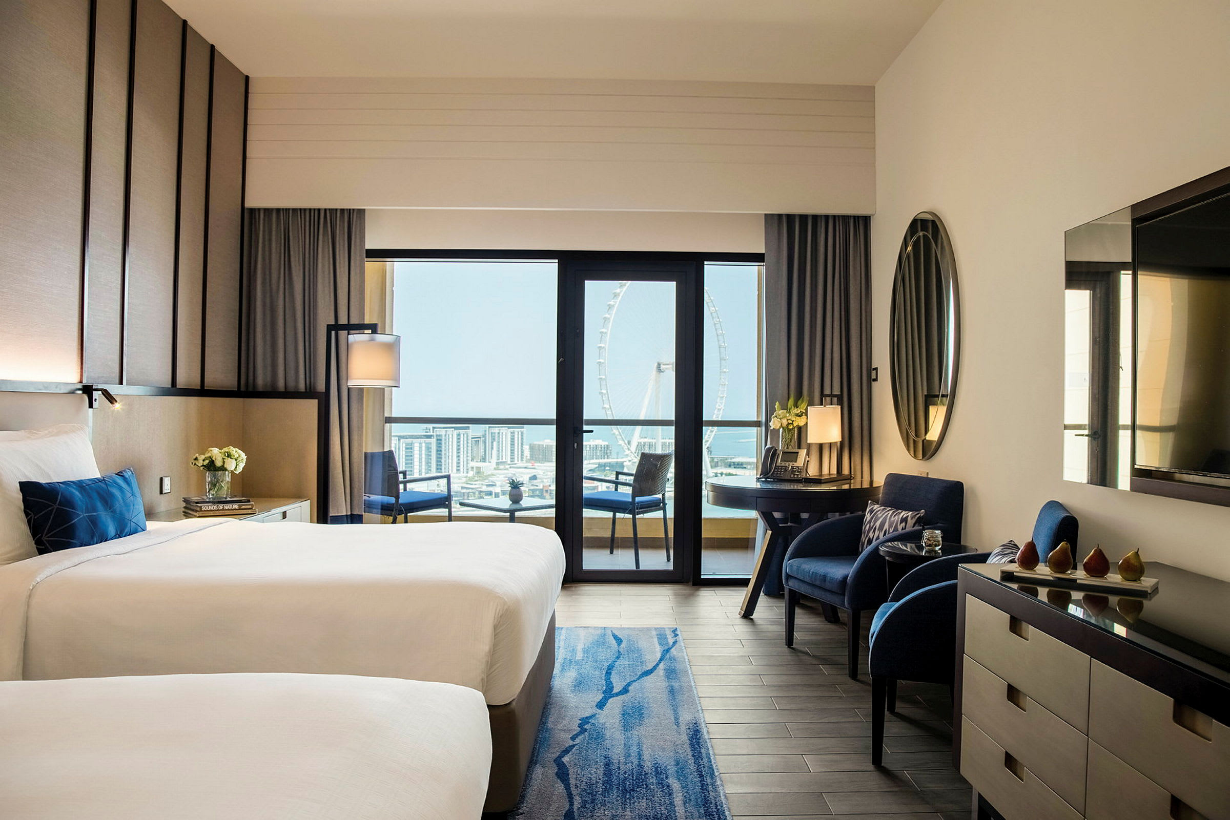 Et moderne hotellrom med to enkeltsenger, enkle møbler og en balkong med utsikt over en by og et stort pariserhjul. (AI-generert tekst)