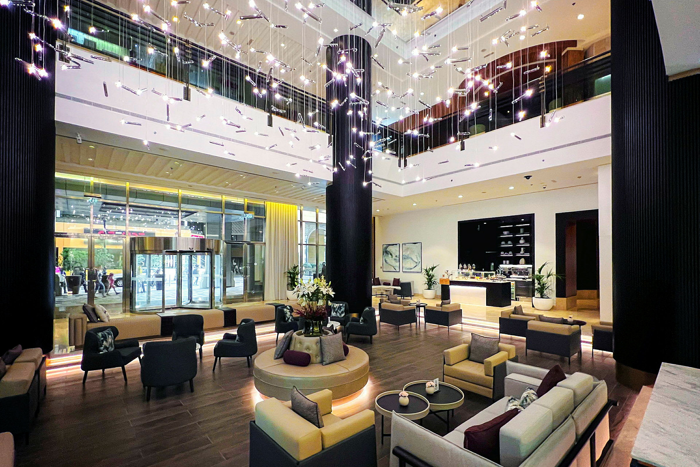 Interiørbilde av et moderne hotellobby med sittegrupper, dekorative lysinstallasjoner og en resepsjon. (AI-generert tekst)
