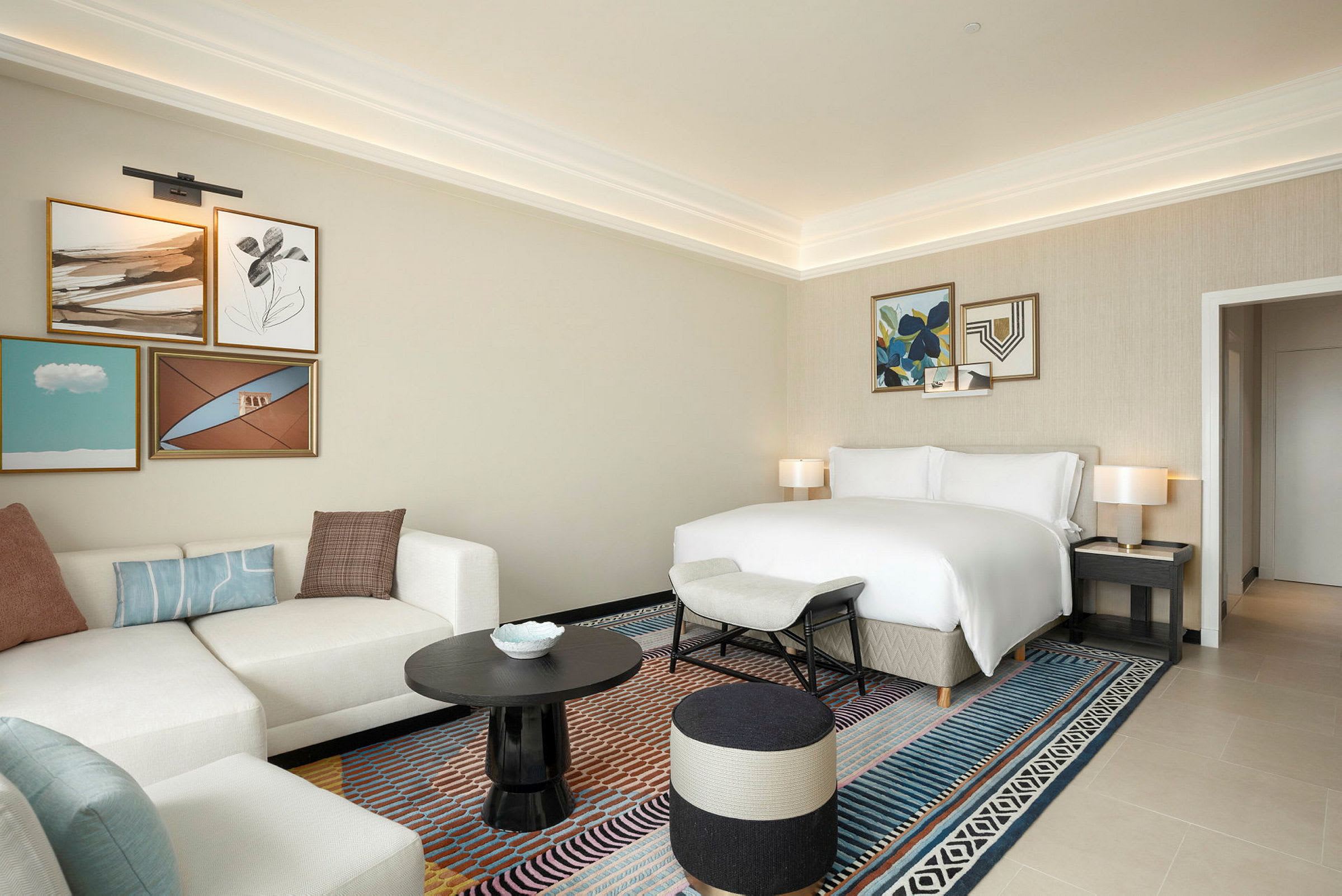 Hotellrom med lys innredning, sofa, seng og kunst på veggene. (AI-generert tekst)