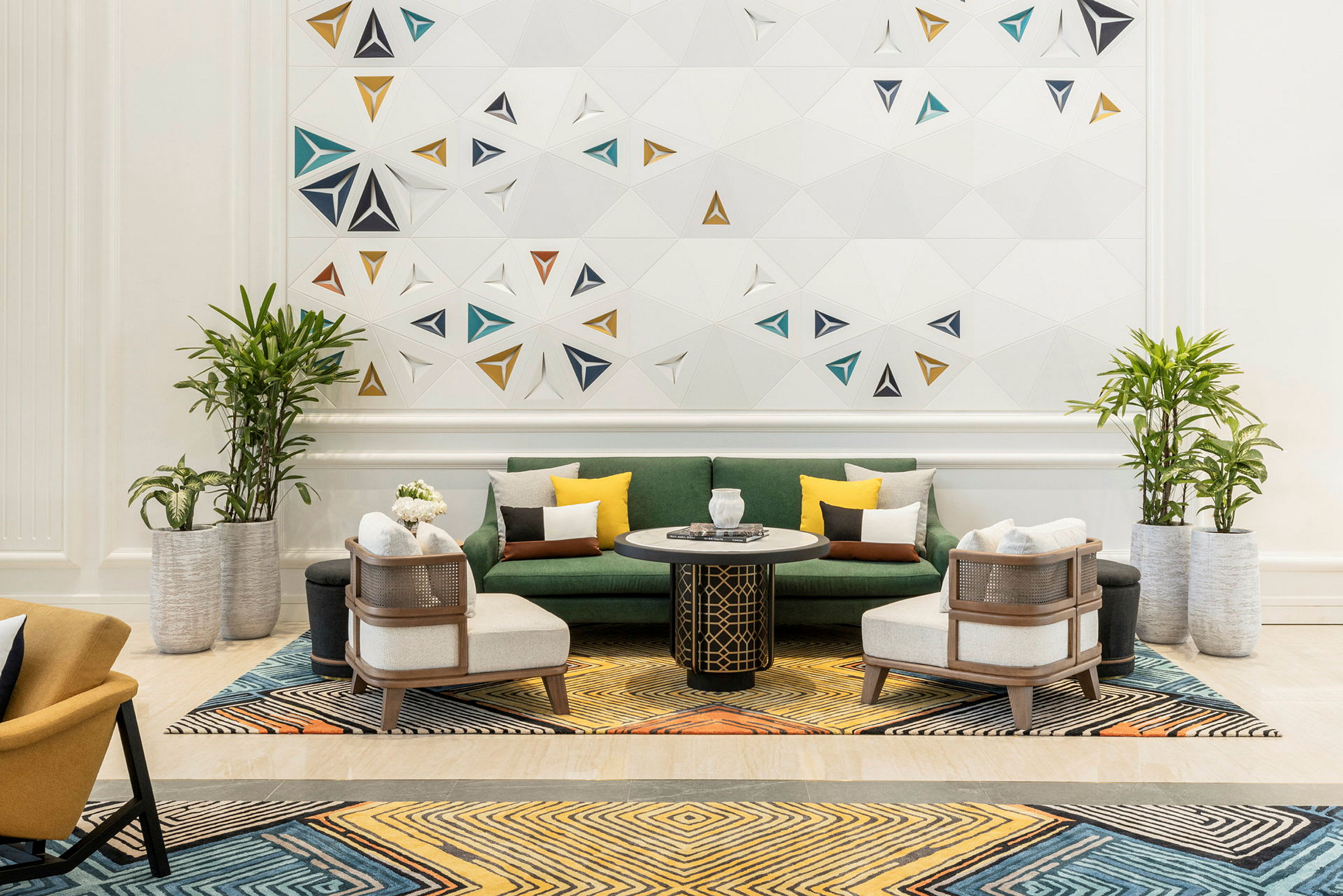 En elegant innredet stue med en grønn sofa, lenestoler og et salongbord på et fargerikt teppe, samt potteplanter og en vegg med geometrisk dekor. (AI-generert tekst)