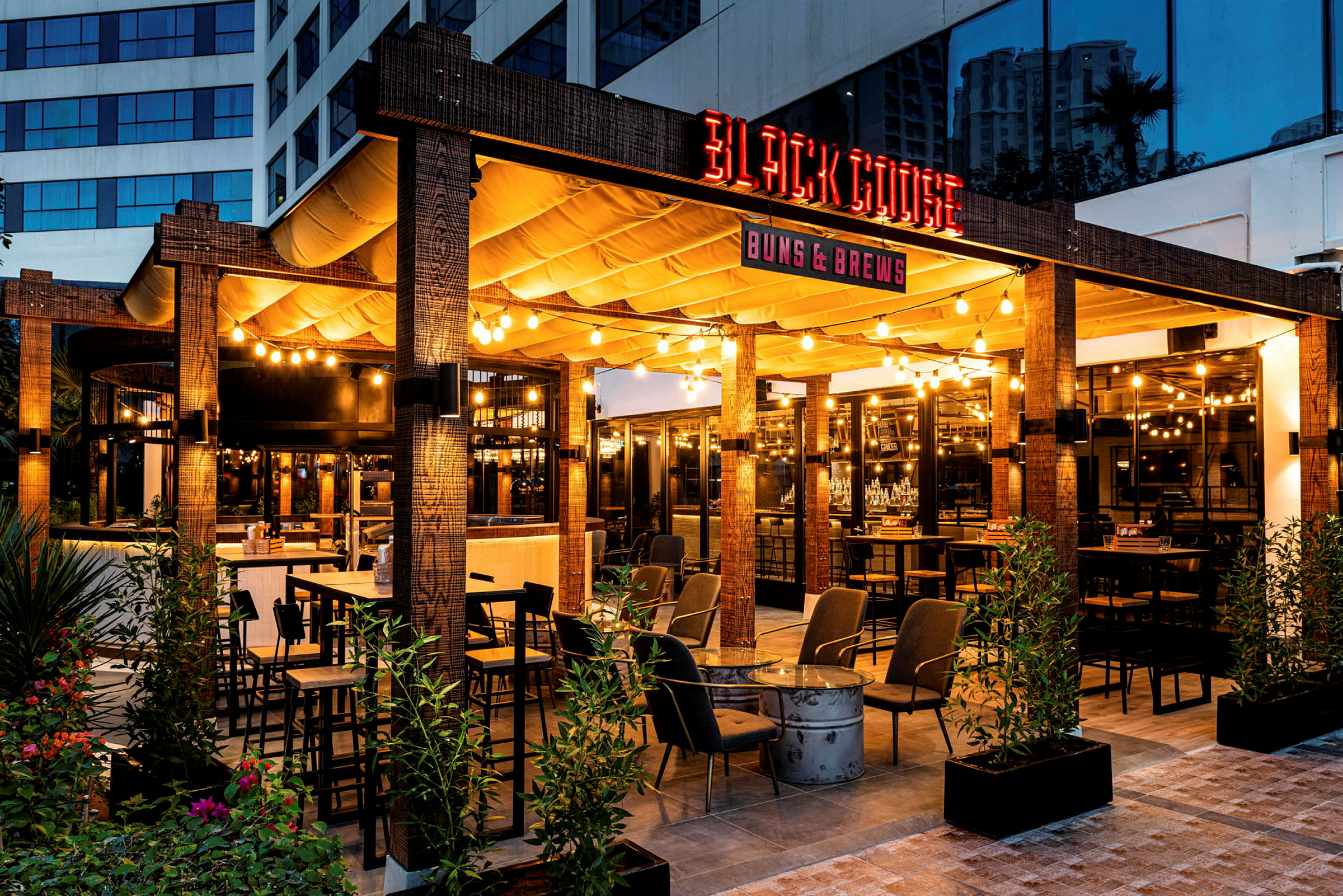 Bilde av en utendørsrestaurant med navnet 'Black Goose', opplyst og dekorativt med møbler og planter. (AI-generert tekst)