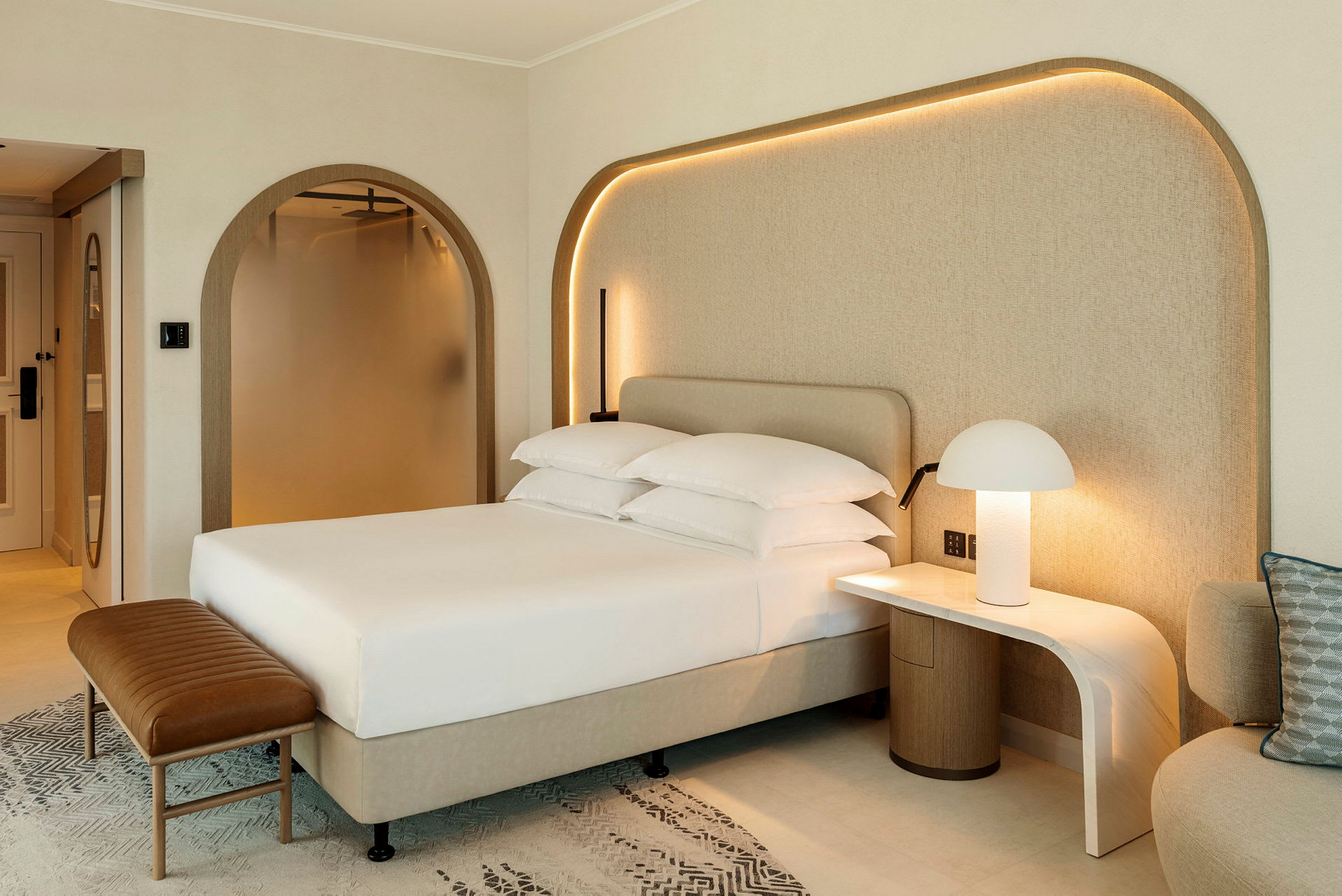 Bilde av et moderne hotellrom med en oppredd seng, nattbord med lampe og en sittemøbel. (AI-generert tekst)