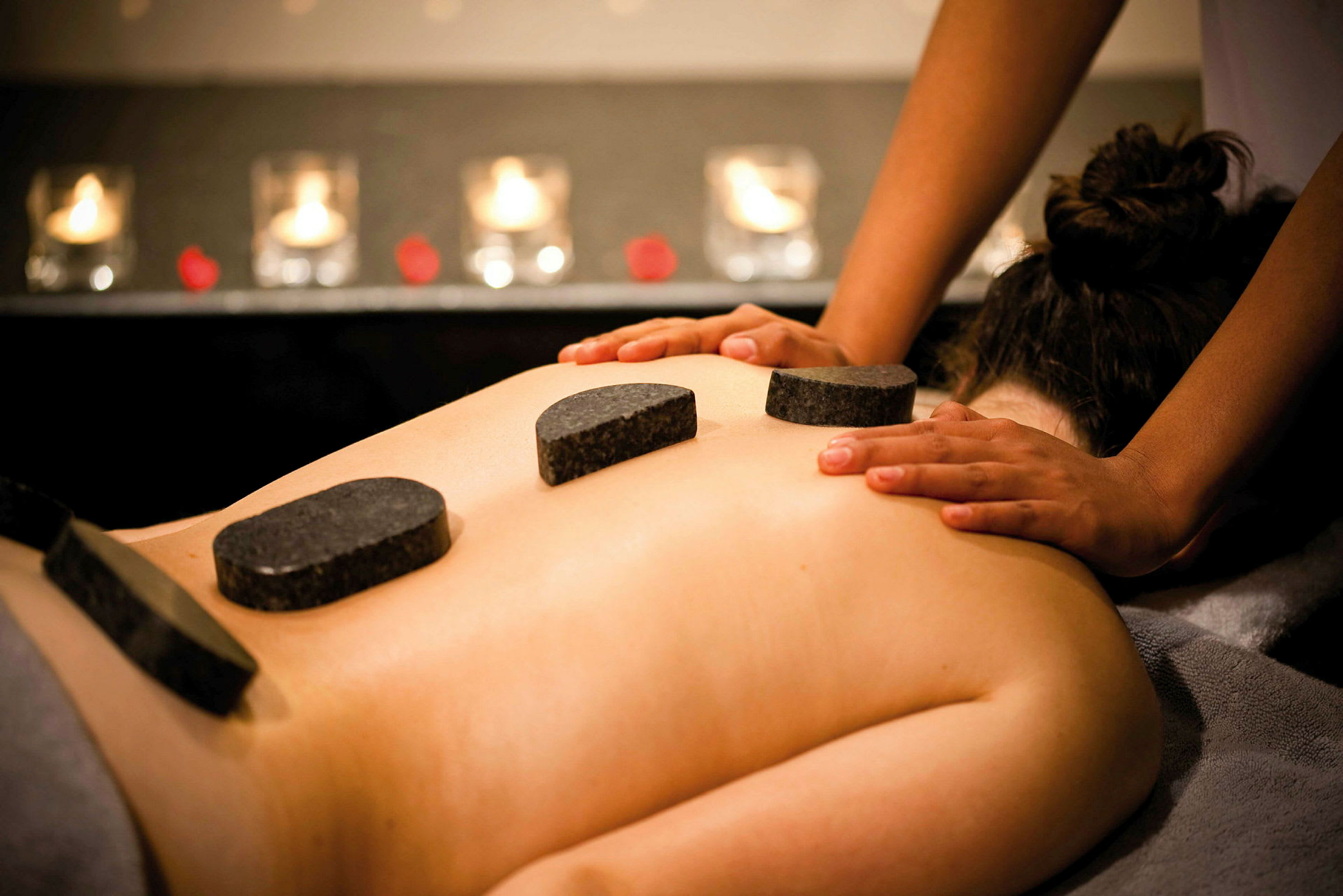En person mottar hot-stone massasje, med varme steiner plassert på ryggen og hender som gir massasje. (AI-generert tekst)