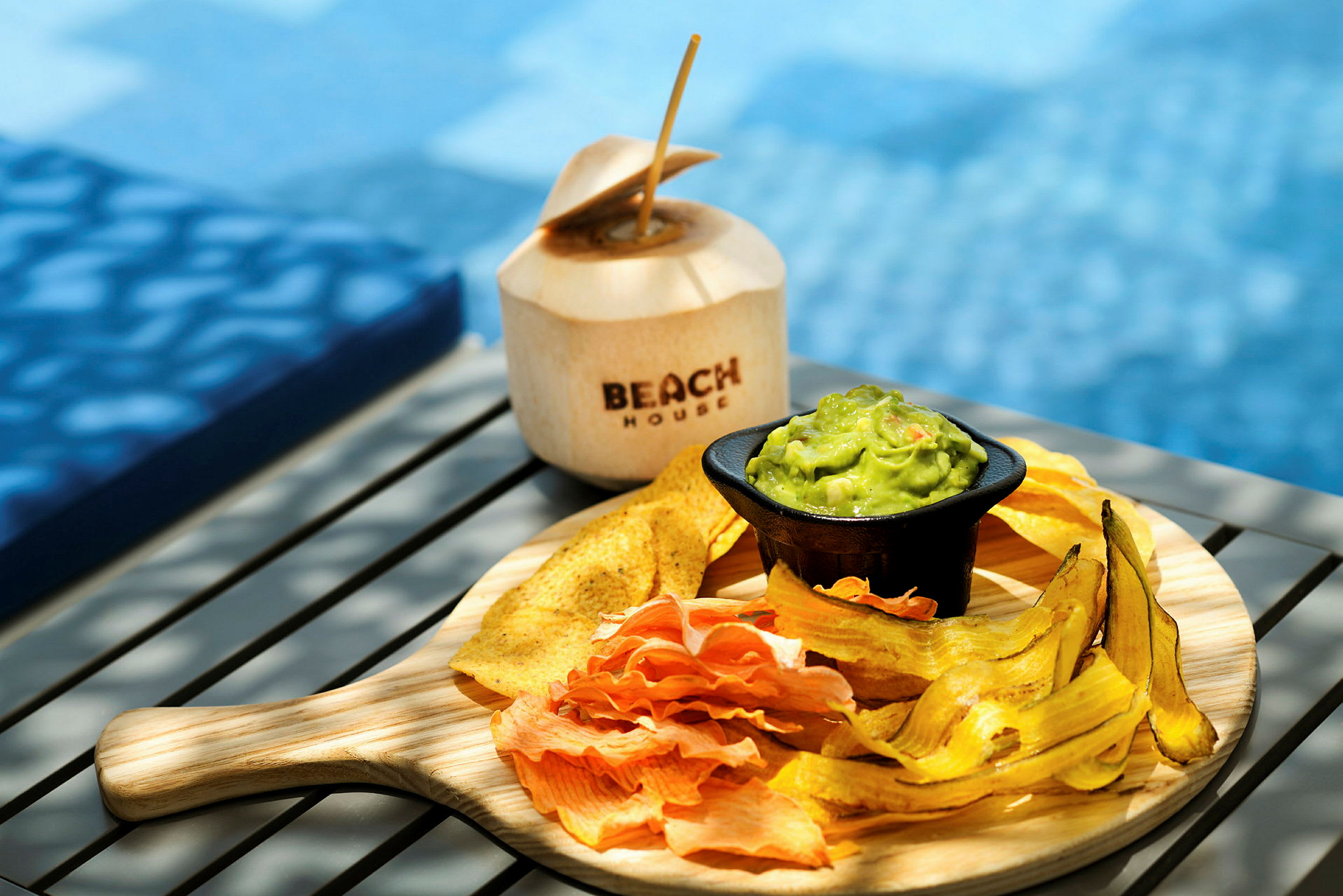 En tallerken med diverse chips og guacamole samt en kokosnøtt med teksten 'Beach House'. (AI-generert tekst)