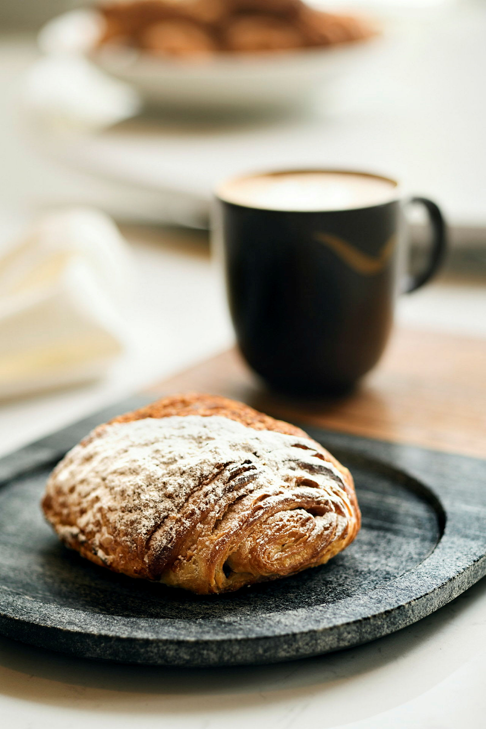 En kopp kaffe og en bolle med melis på et fat. (AI-generert tekst)