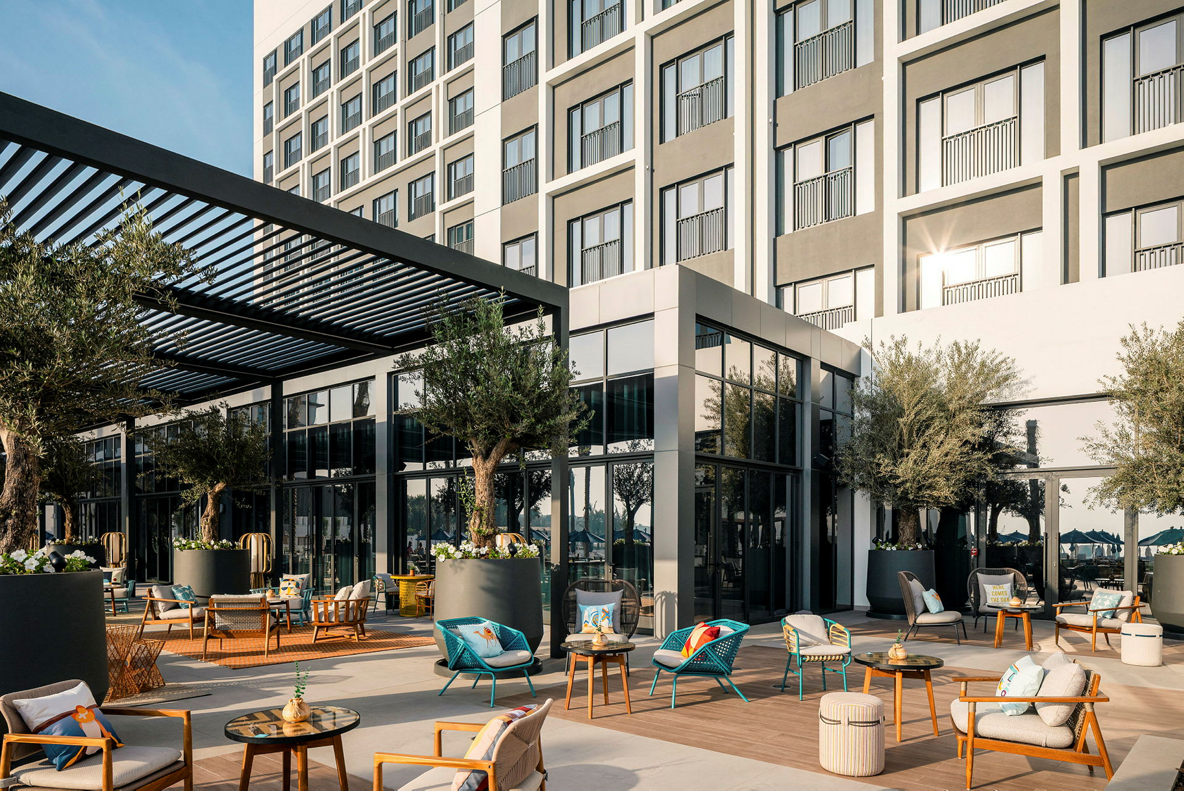 Hotellfasade med møblert uteplass, skyggelagt av en pergola, omgitt av planter. (AI-generert tekst)