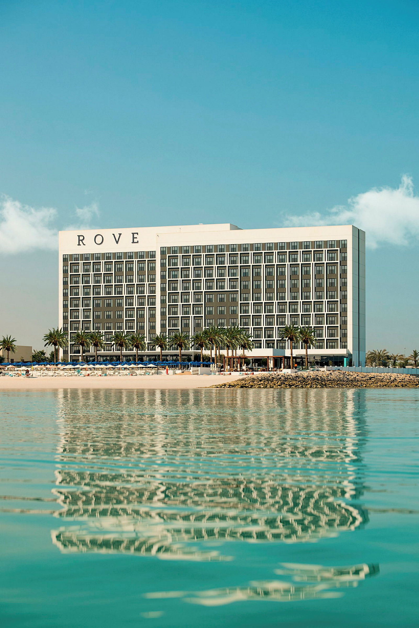 Hotellet Rove ved stranden med palmer og vann. (AI-generert tekst)