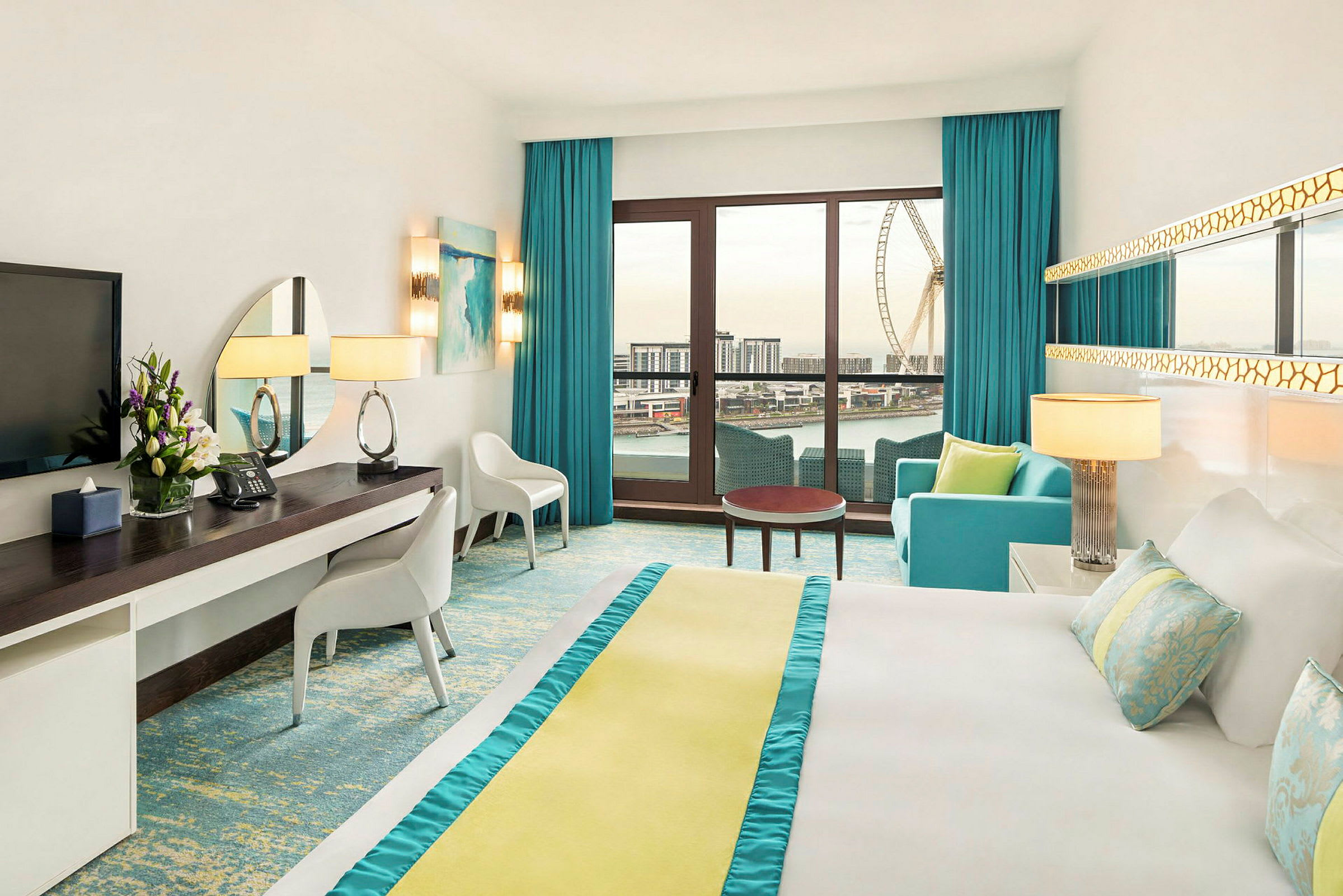 Moderne hotellrom med lyse farger, stor seng, skrivebord og sitteområde. Et stort vindu med utsikt over en stor by og et pariserhjul. (AI-generert tekst)