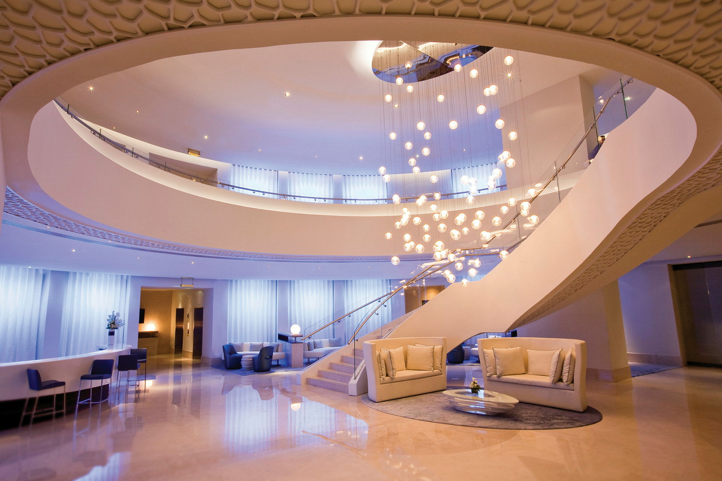 En elegant hotellobby med en stor lysekrone, moderne sofaer og en åpen etasjeplan. (AI-generert tekst)