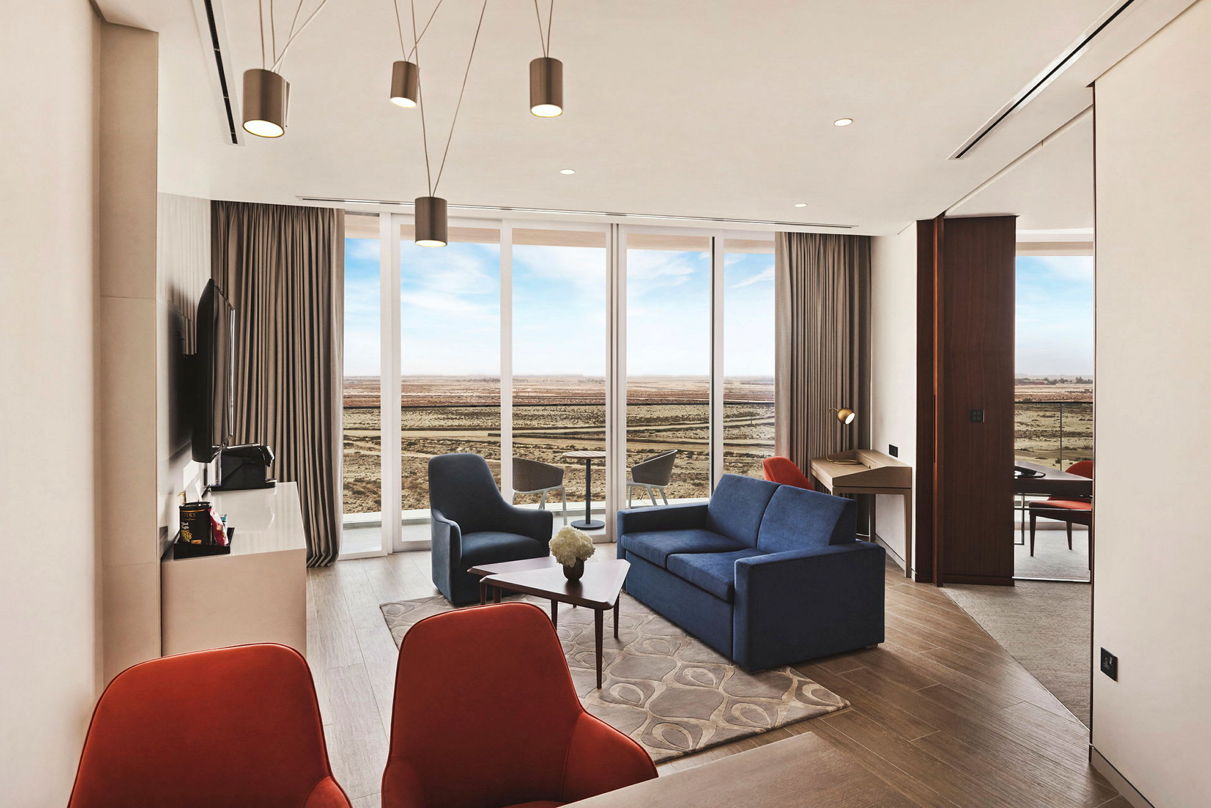 Et moderne hotellrom med en sittegruppe, store vinduer som vender ut mot et åpent landskap og et skrivebord. (AI-generert tekst)