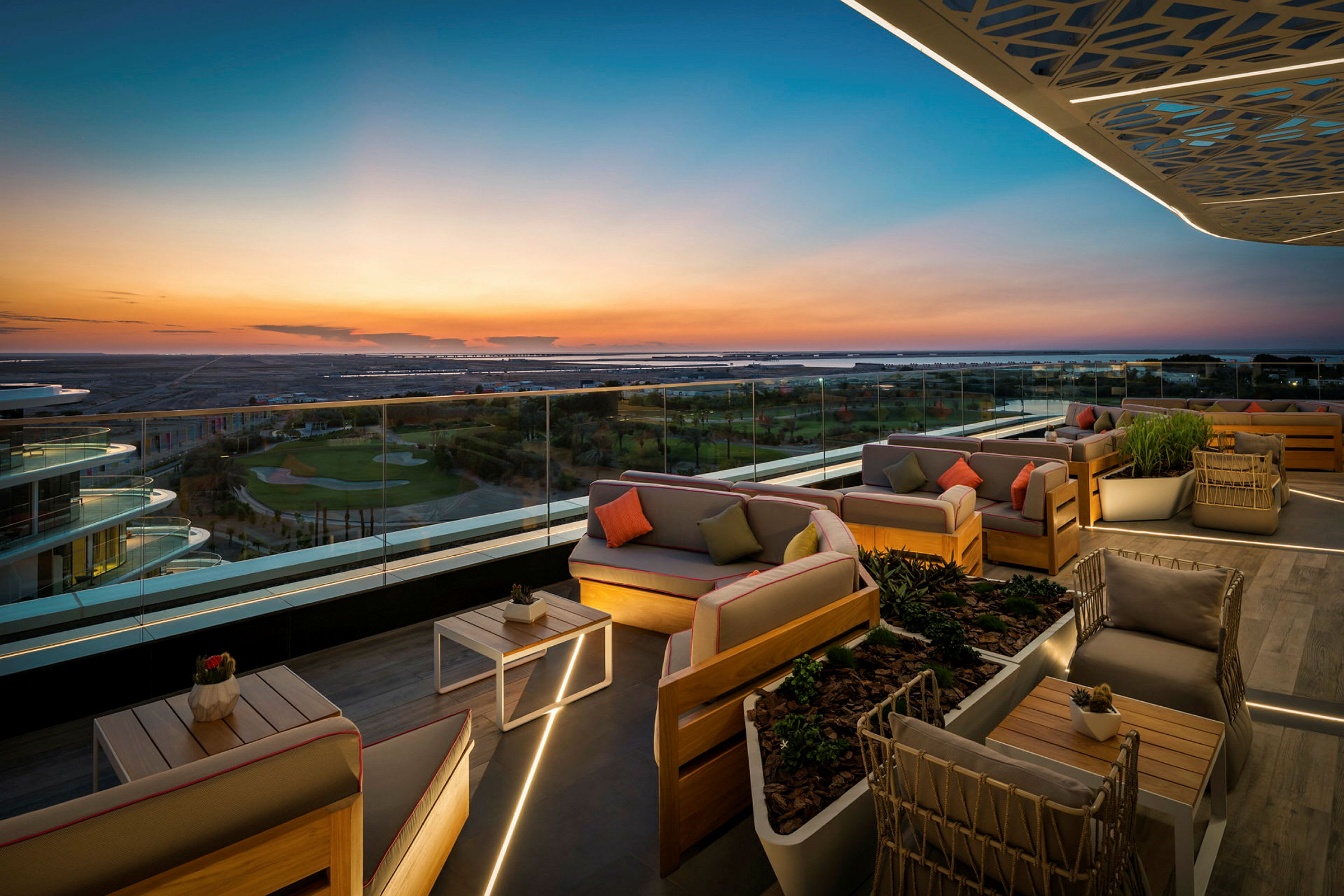 En takterrasse med elegante sittemøbler og glassrekkverk som gir panoramautsikt over landskapet i solnedgang. (AI-generert tekst)