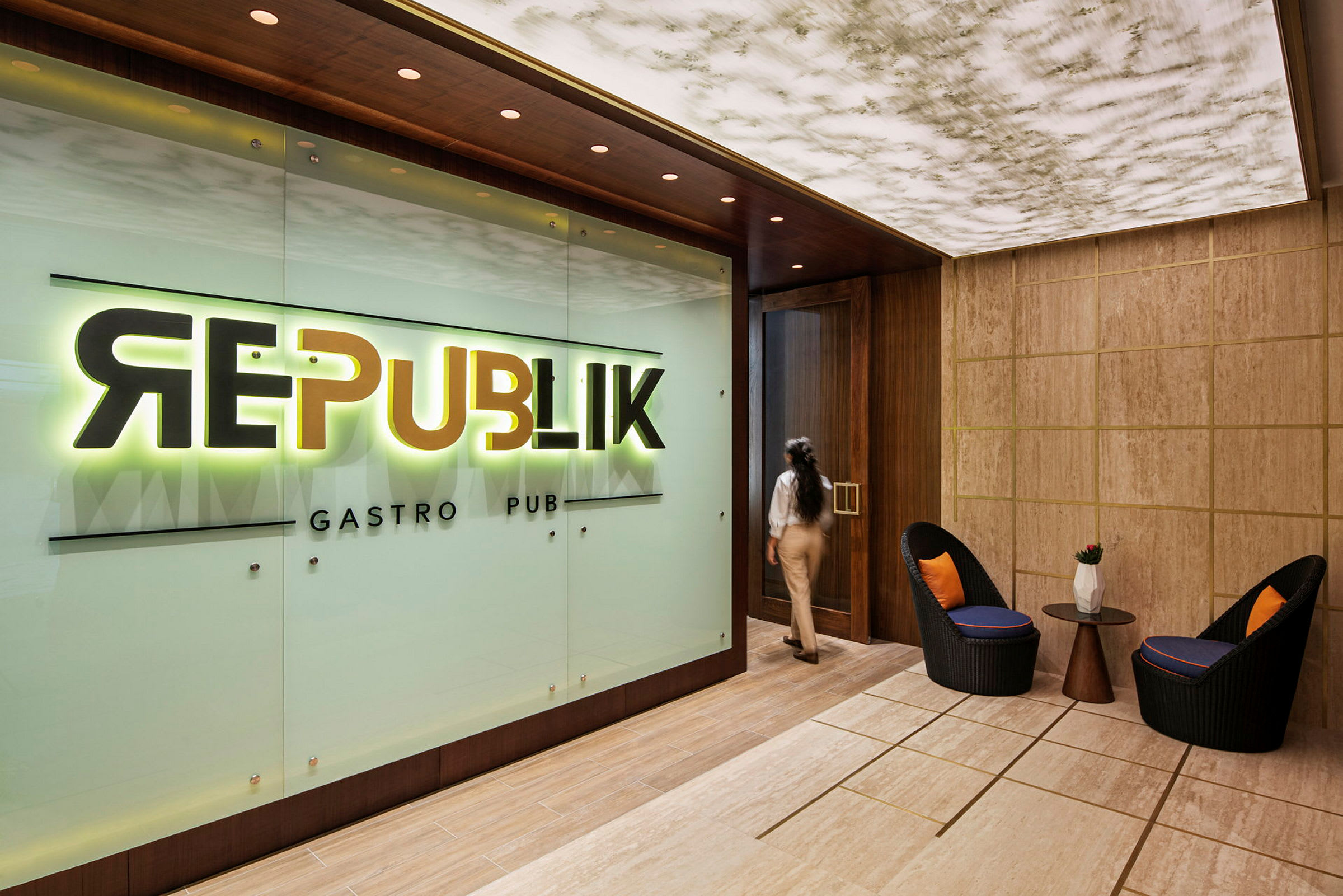 Inngangen til en restaurant eller bar med et skilt som sier "Republik Gastro Pub". I forgrunnen er det to stoler og et bord. (AI-generert tekst)