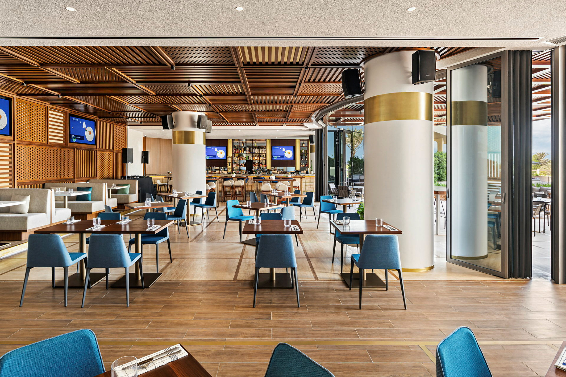 En moderne restaurant med trematerial i taket, blå stoler og dekte bord. (AI-generert tekst)