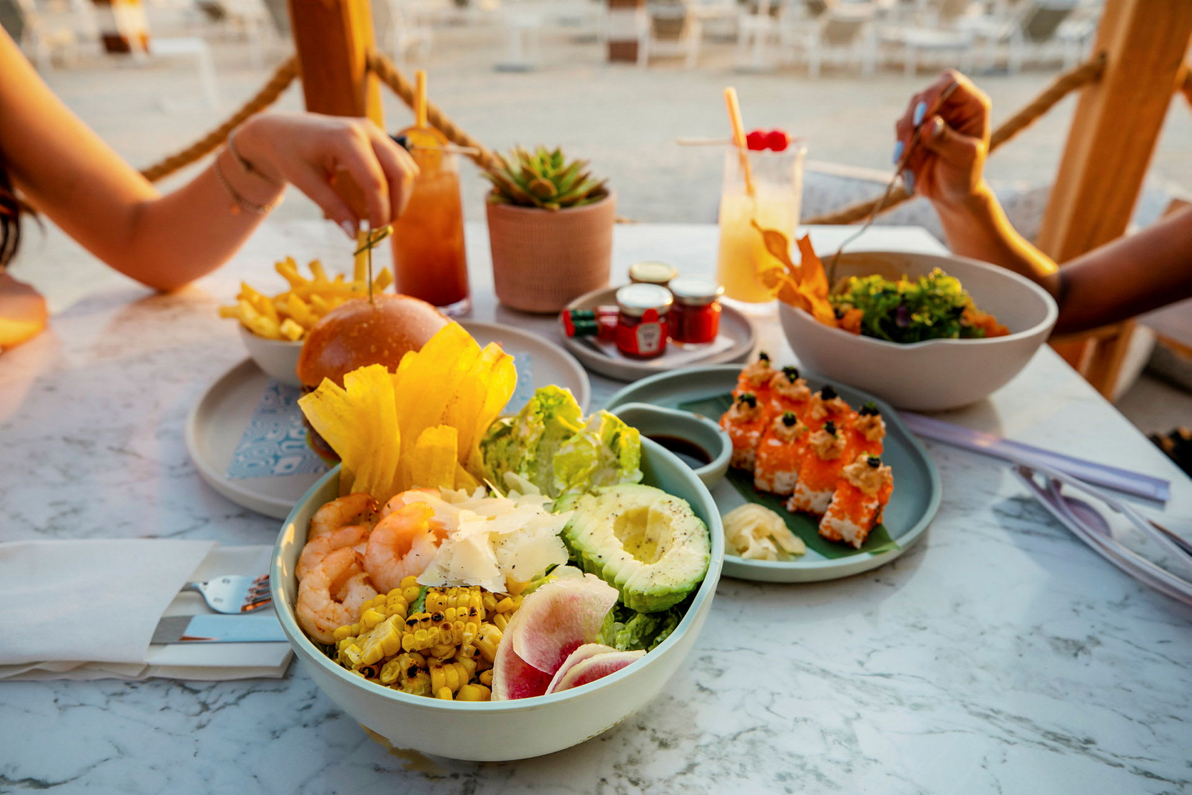Et bord fylt med ulike retter inkludert salat, sushi, hamburger og drikke. (AI-generert tekst)