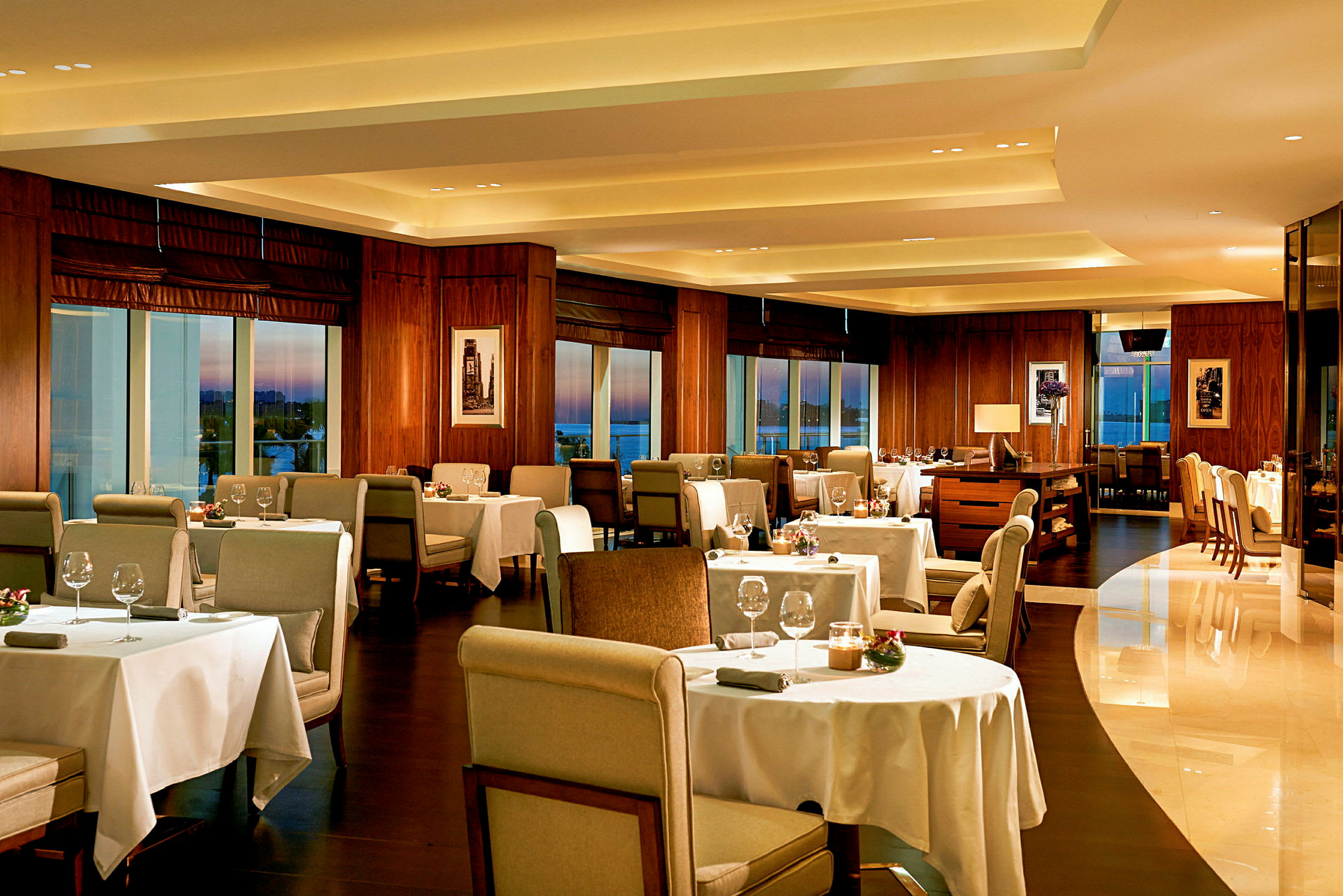 Elegant restaurant med bord dekket med hvite duker, stoler og dekorasjoner, samt store vinduer med utsikt. (AI-generert tekst)