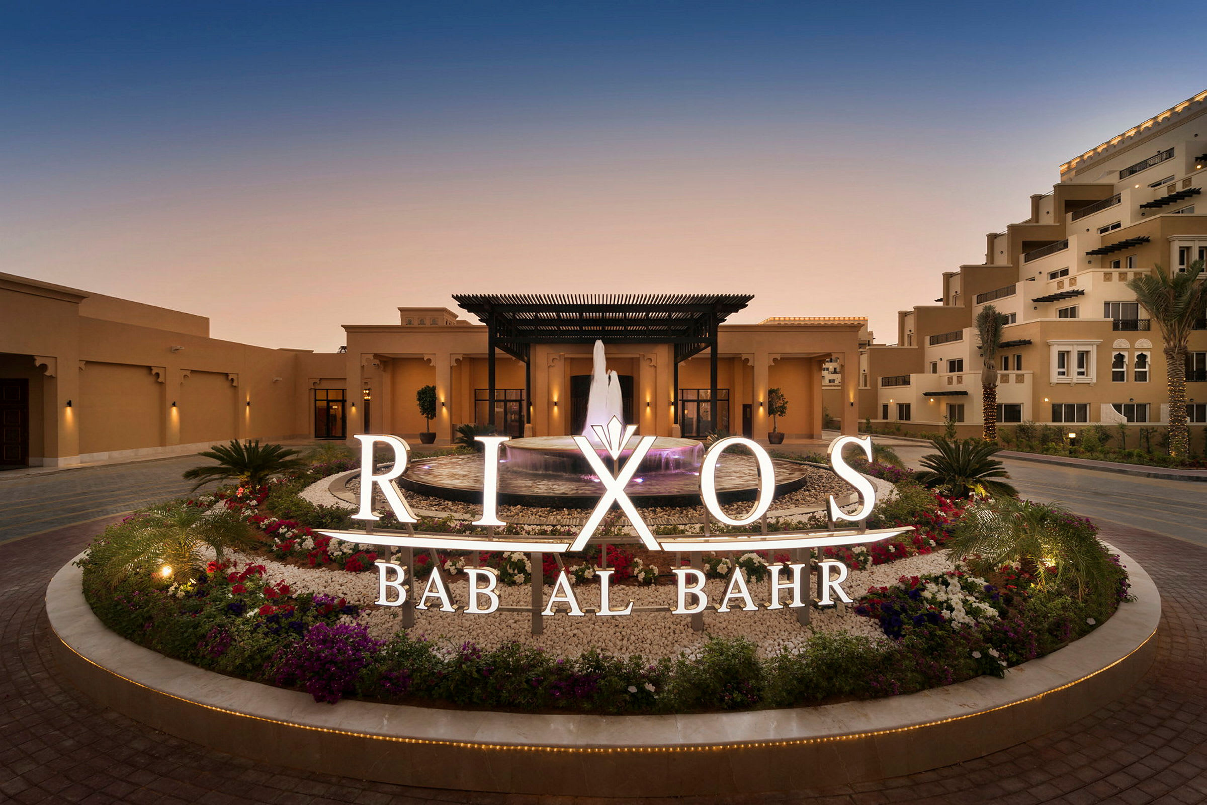 Hotellinngang med fontene og omkringliggende blomster, skilt med teksten Rixos Bab Al Bahr. (AI-generert tekst)